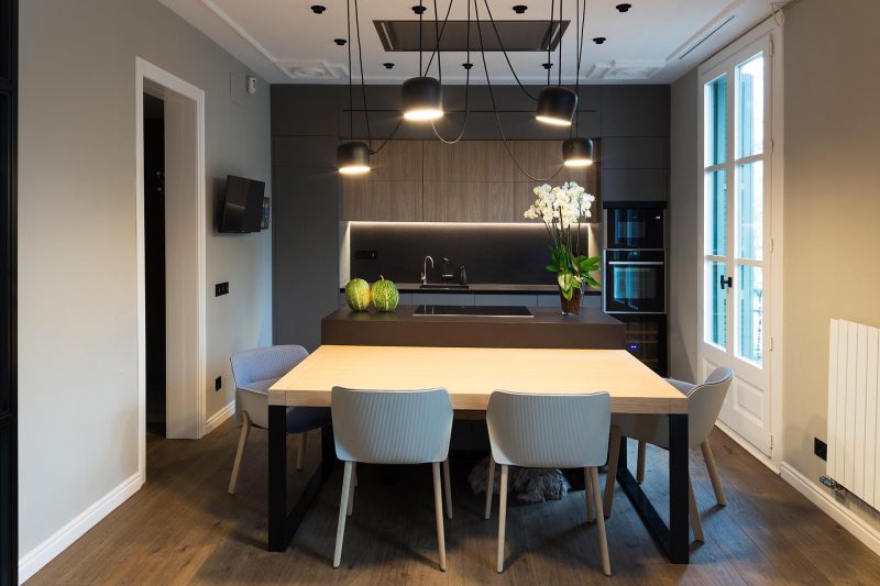 This modern flexible kitchen and dining room has dark cabinetry and island, which is contrasted by the light wood dining table, which can be moved.