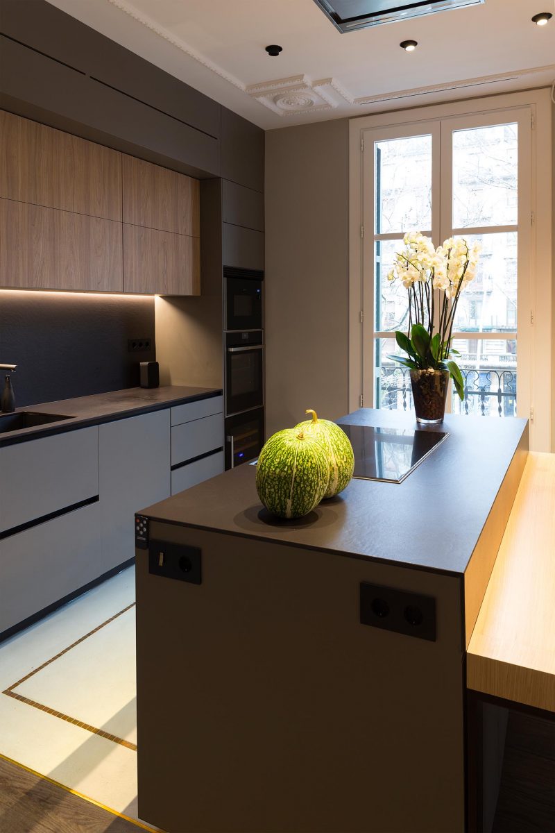 A modern kitchen with dark gray and wood cabinets, and a black countertop.