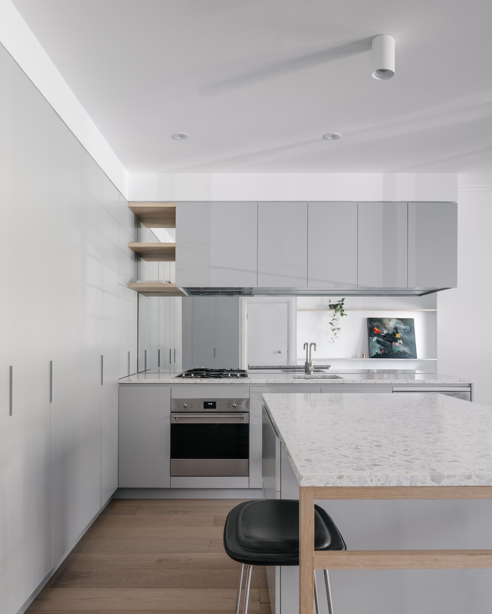 A modern kitchen with minimalist gray cabinets, white stone countertops, and oak flooring.