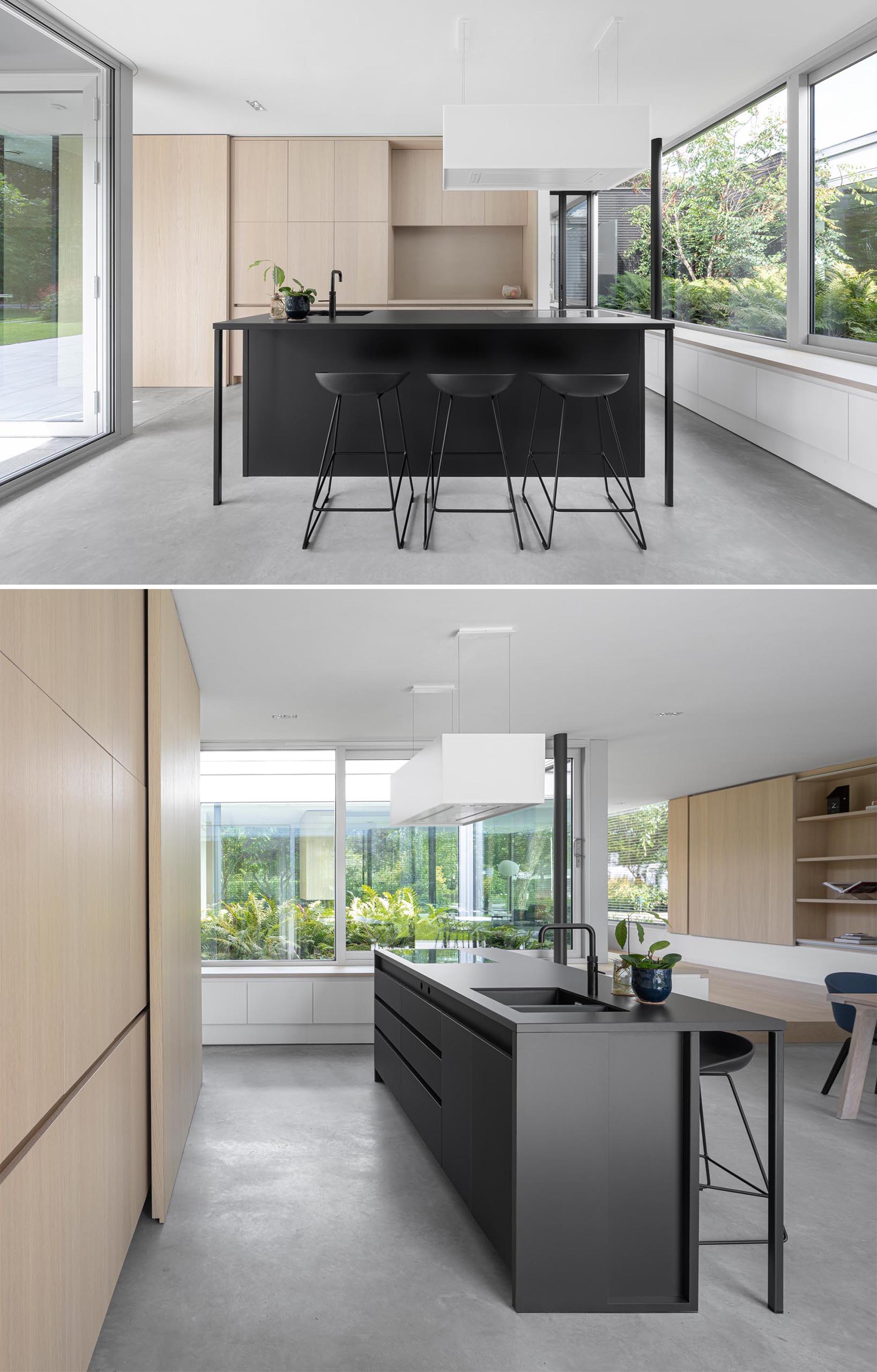 A modern kitchen with minimalist wood cabinets, a matte black island with matching stools, and concrete floors.