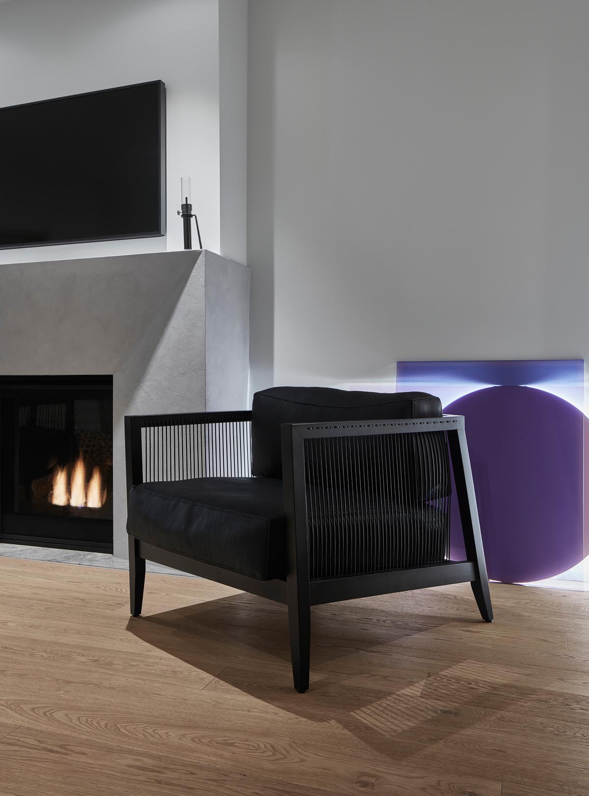 A modern living room with a black armchair, a grey fireplace surround, and wood floors.