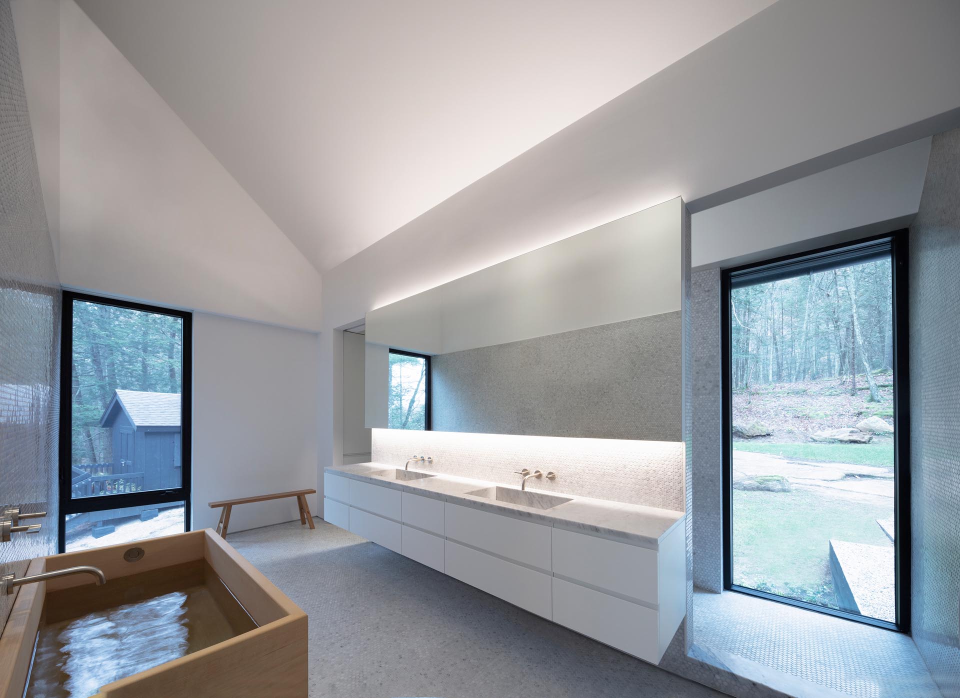 A modern master bathroom with a wood soaking tub, a backlit mirror, a double-sink floating vanity, and a sloped ceiling.