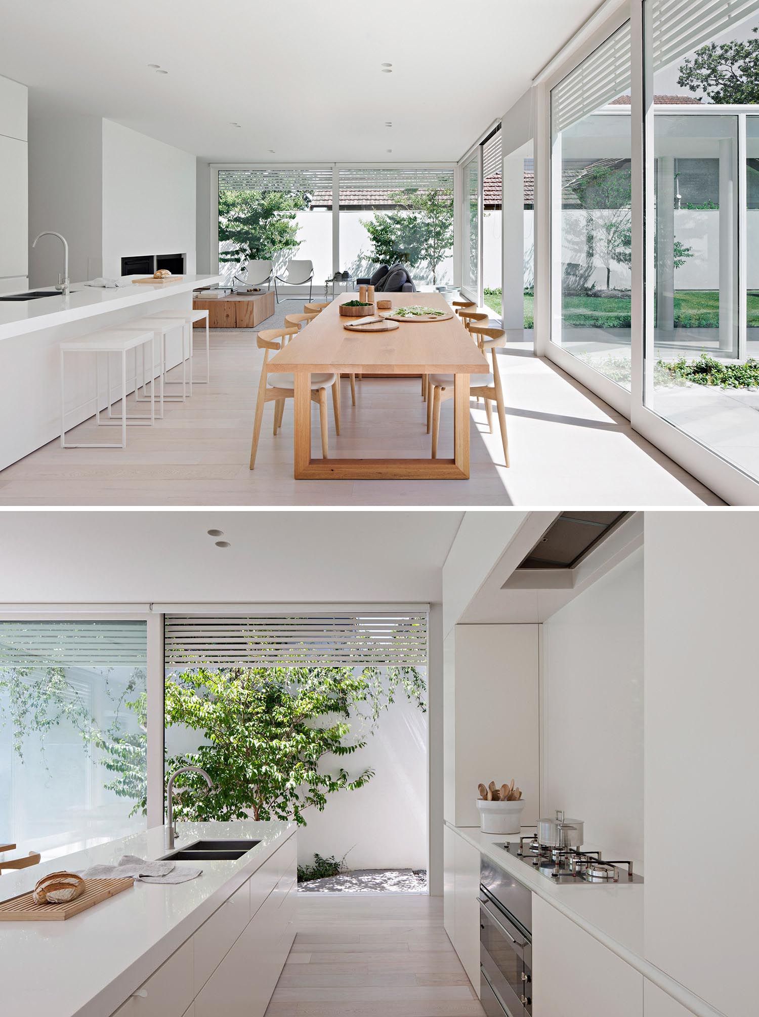 A modern open plan interior with a large wood dining table and minimalist white kitchen.