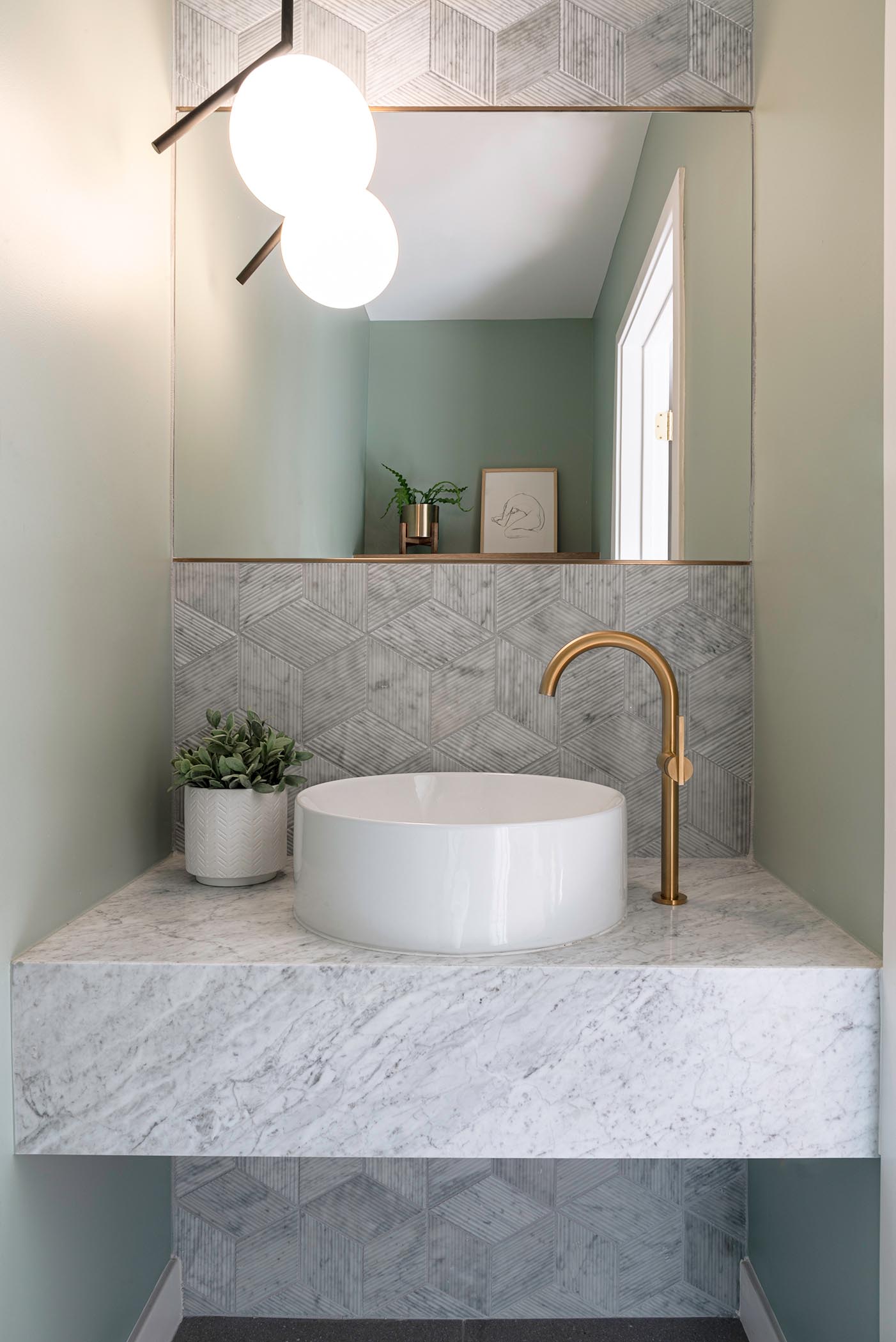 In this small but modern powder room, tile with a textural bamboo-like finish covers the wall, while a floating vanity is topped with a round white vessel sink and bronze accents.