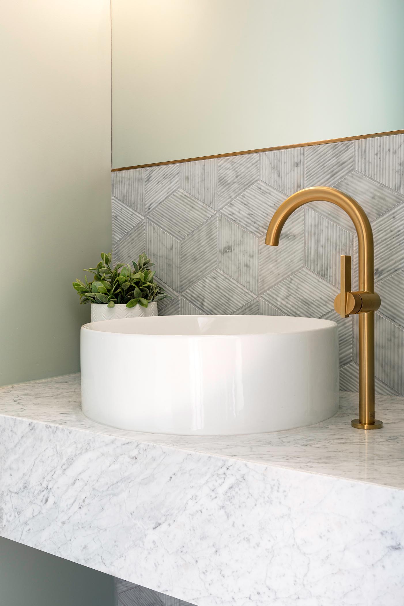 In this small but modern powder room, tile with a textural bamboo-like finish covers the wall, while a floating vanity is topped with a round white vessel sink and bronze accents.