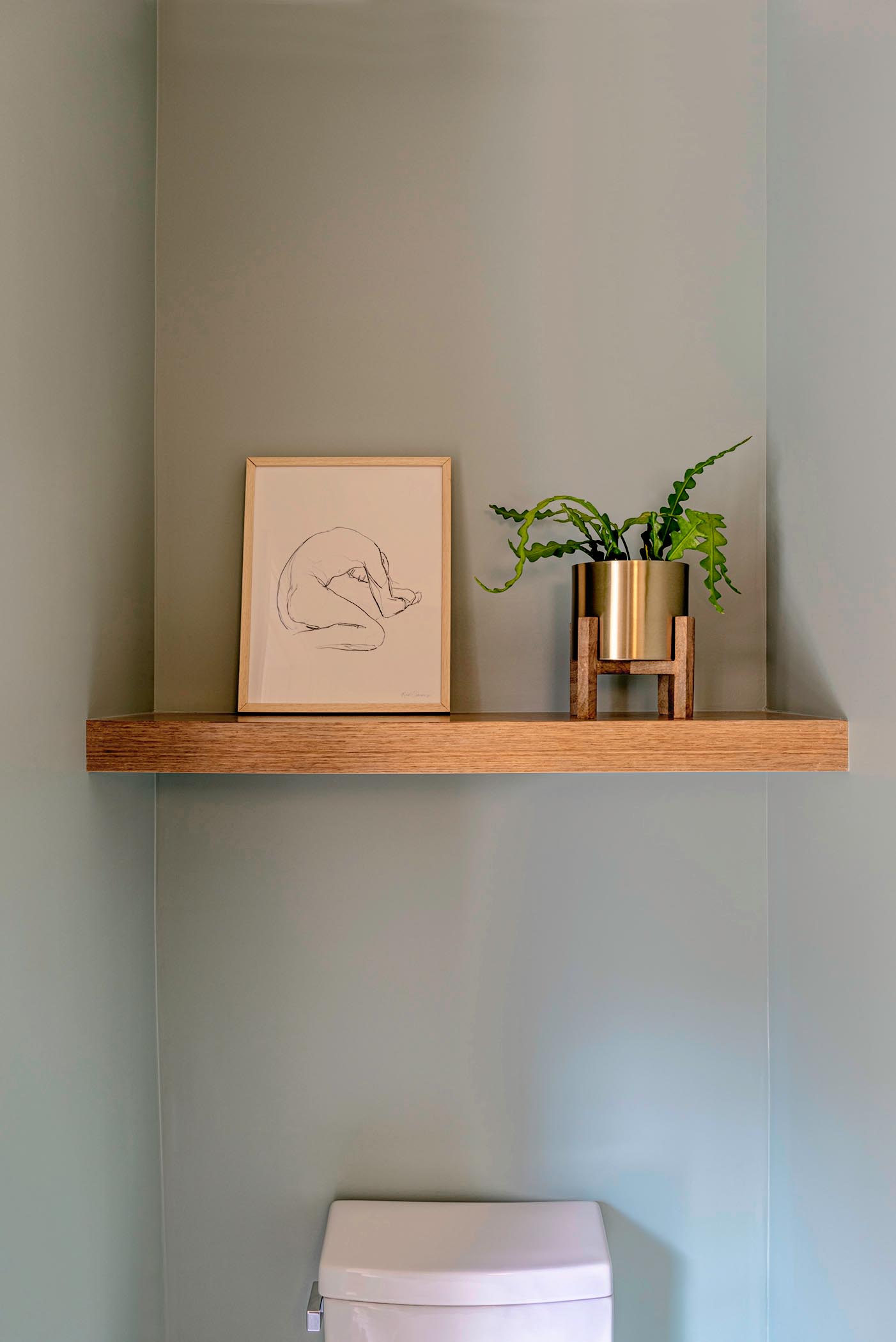 A small powder room with a single wood shelf that showcases art and a plant.