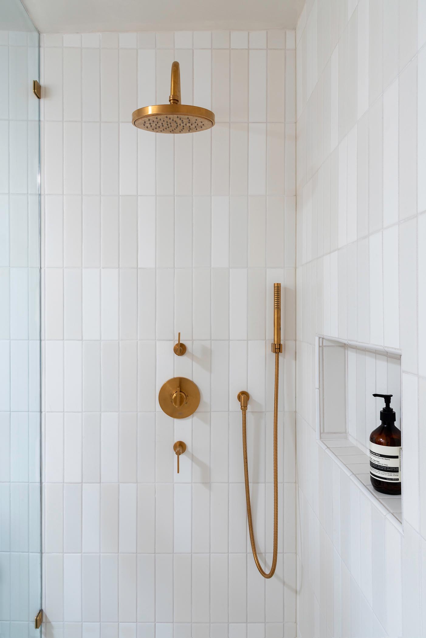 A modern white shower with a shelving niche and brass hardware.