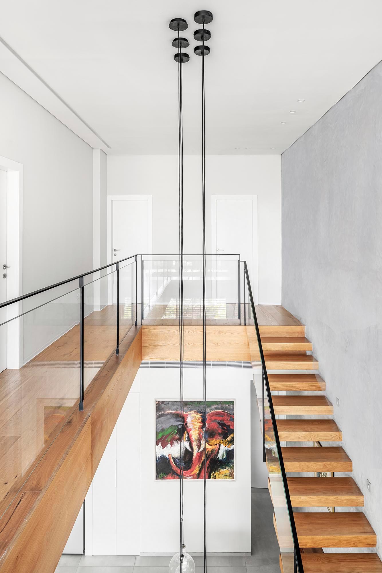 The top of this wood staircase opens to a walkway that leads to a small sitting room. The railing, composed of iron and glass, completes the clean and minimalist look.