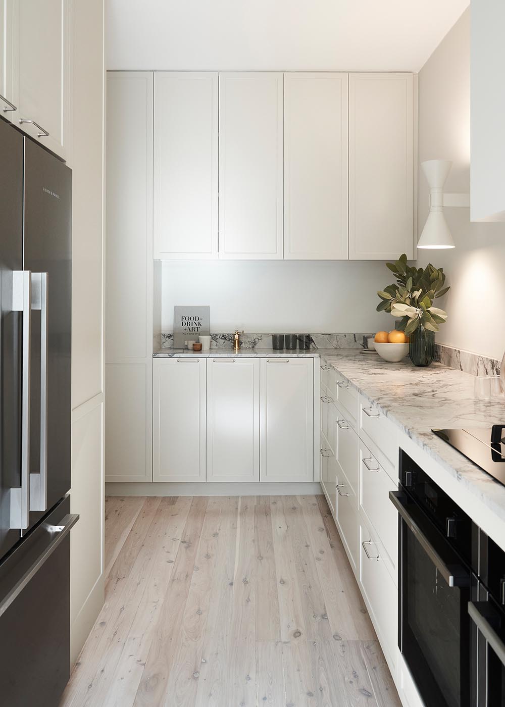 This contemporary kitchen features stone counters, warm textures, handmade tiles, and pale toned cabinetry that complement the other design choices throughout the apartment.