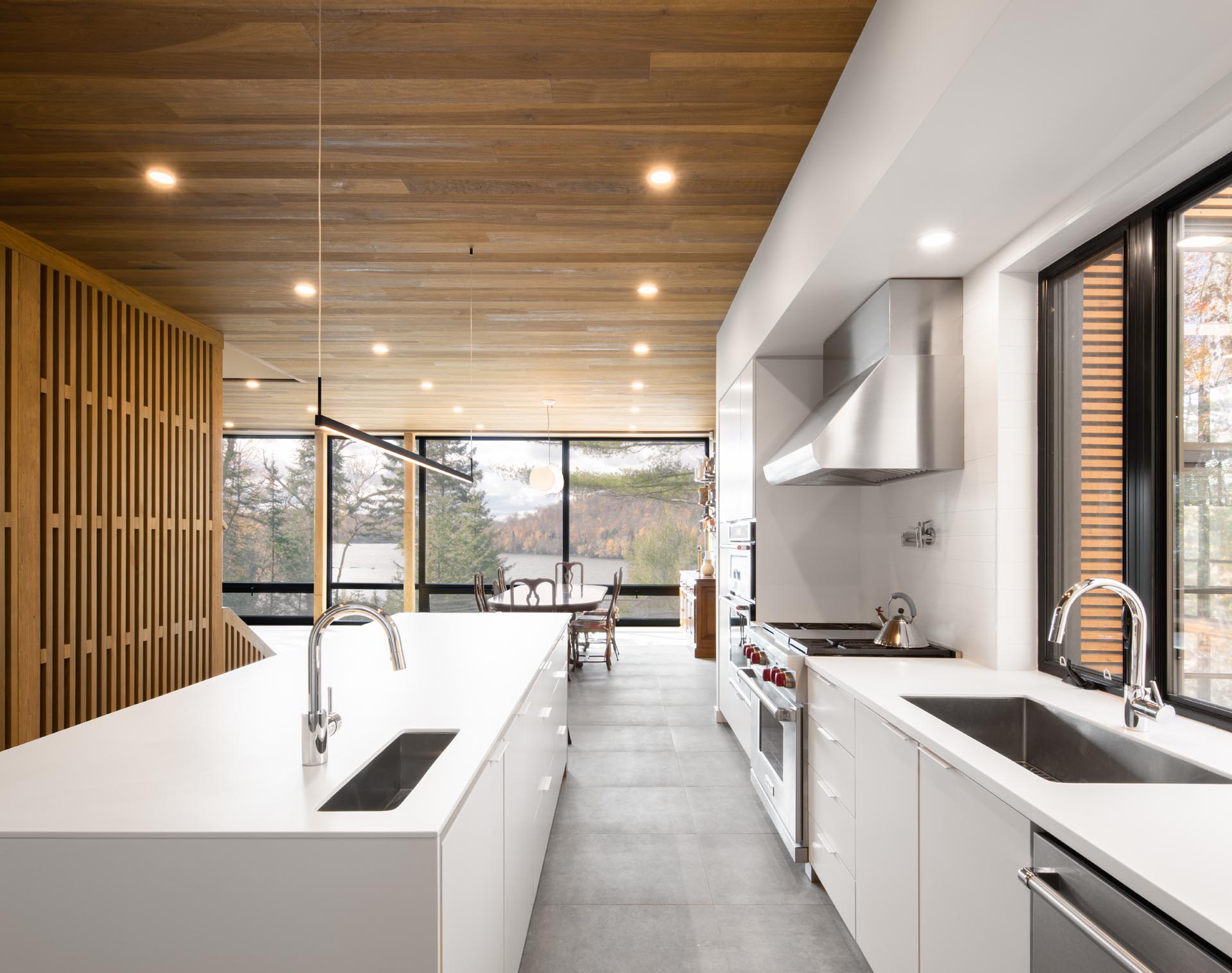 A large white kitchen with an island and an open plan dining area both enjoy views of the lake through floor-to-ceiling windows.