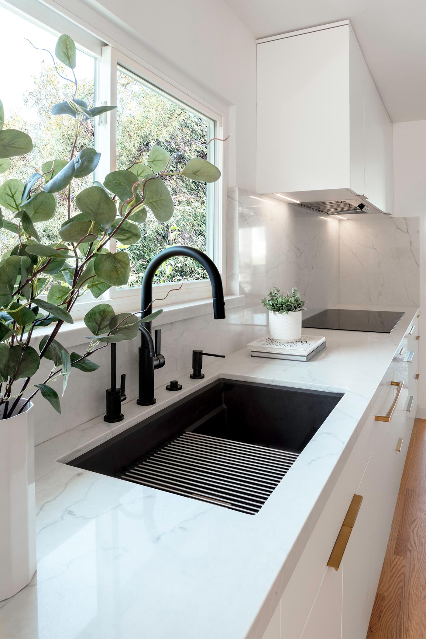 This matte black kitchen sink, which sits below the window, has a matching black faucet and hardware, while the cabinetry hardware adds a luxurious metallic touch.
