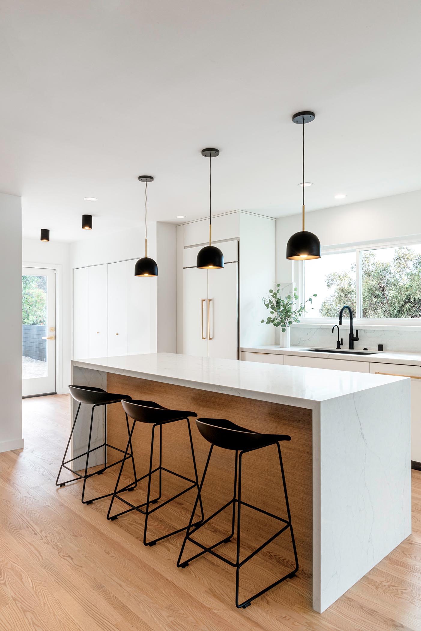 Three black pendant lights by Cedar & Moss hang above a modern kitchen island which complement the black stools. The design of the island allows the stools to be neatly tucked away when not being used. 