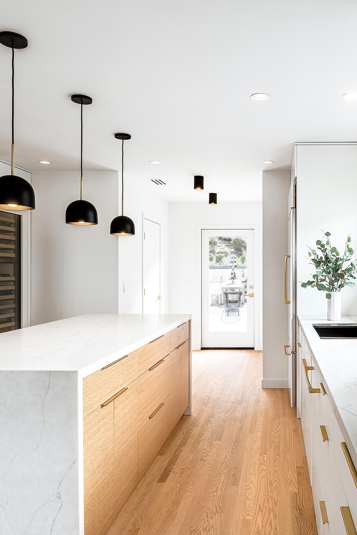 The open concept kitchen has white and wood cabinets and an island with a custom waterfall quartz countertop.