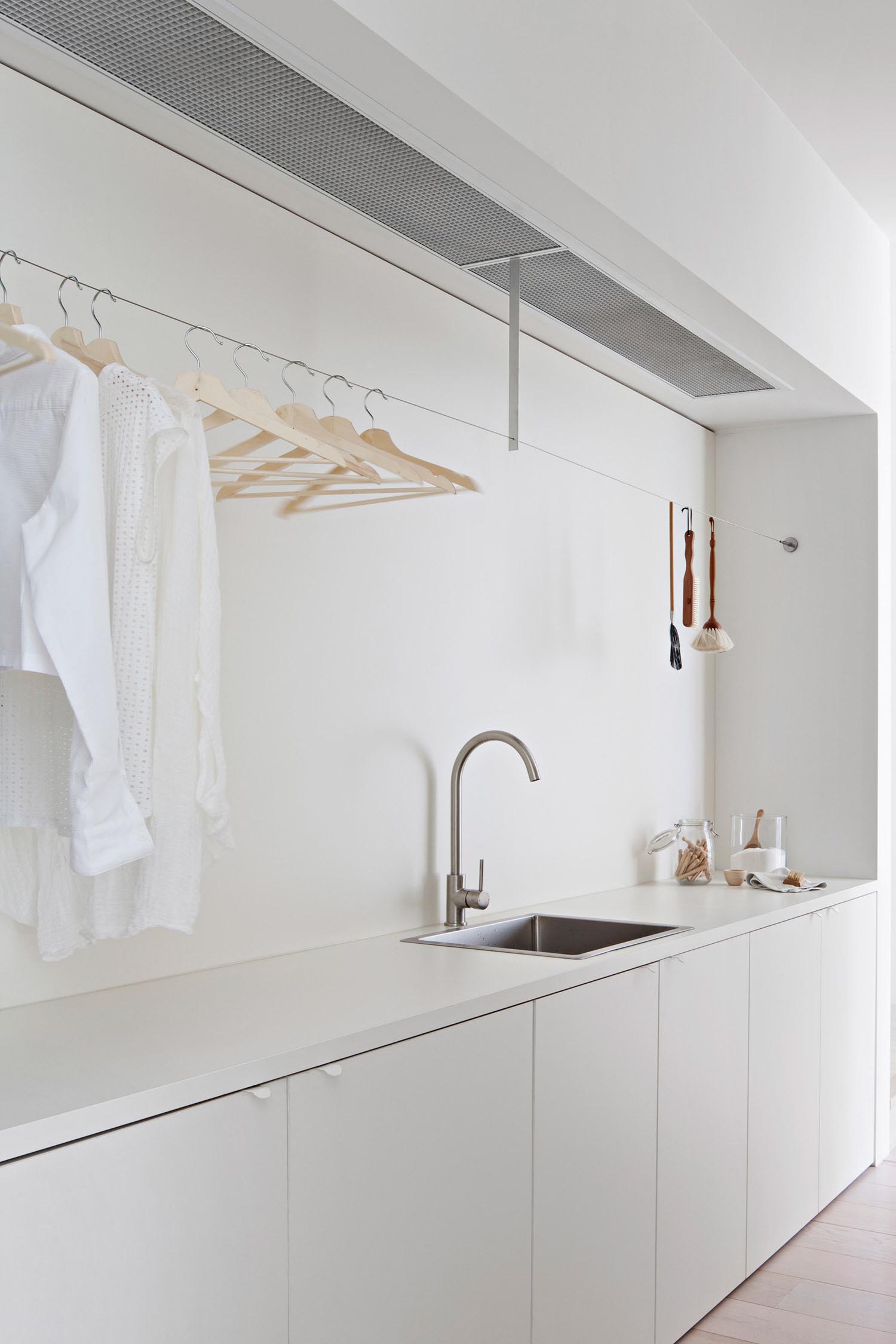 A modern white laundry room with sink, cabinets, and a place to hang clothes to dry.