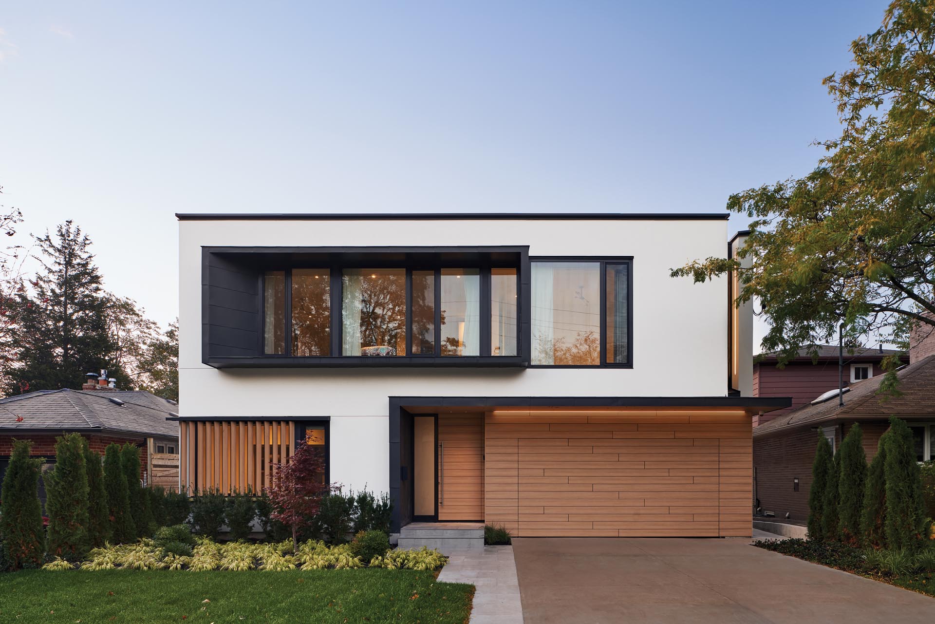 The exterior of this modern house features a facade of white stucco walls and black metal accent panels, which were paired with warm oak-look phenolic panels.