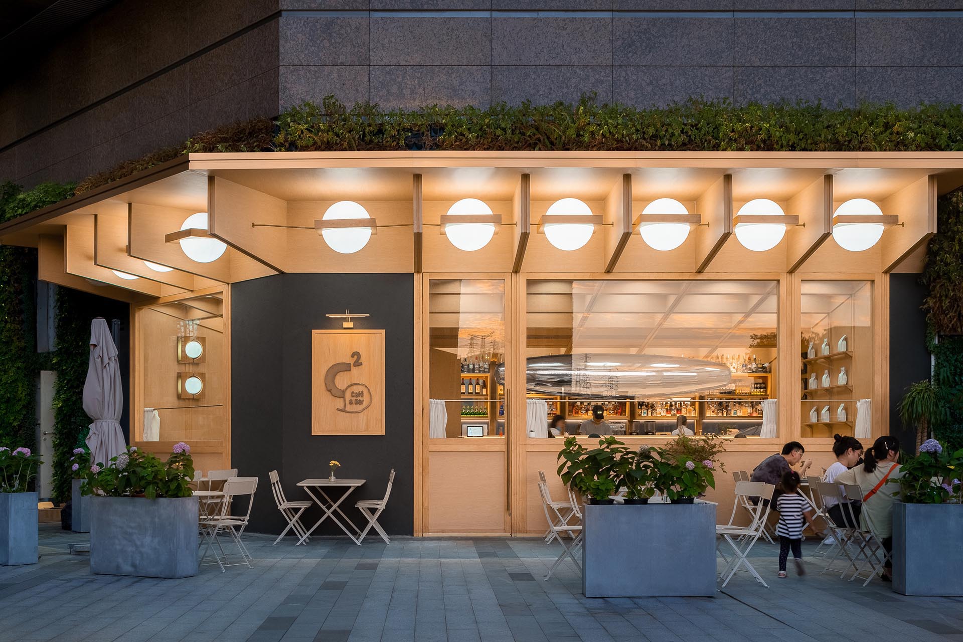 A modern cafe and bar with a wood exterior, outdoor seating, and large windows.