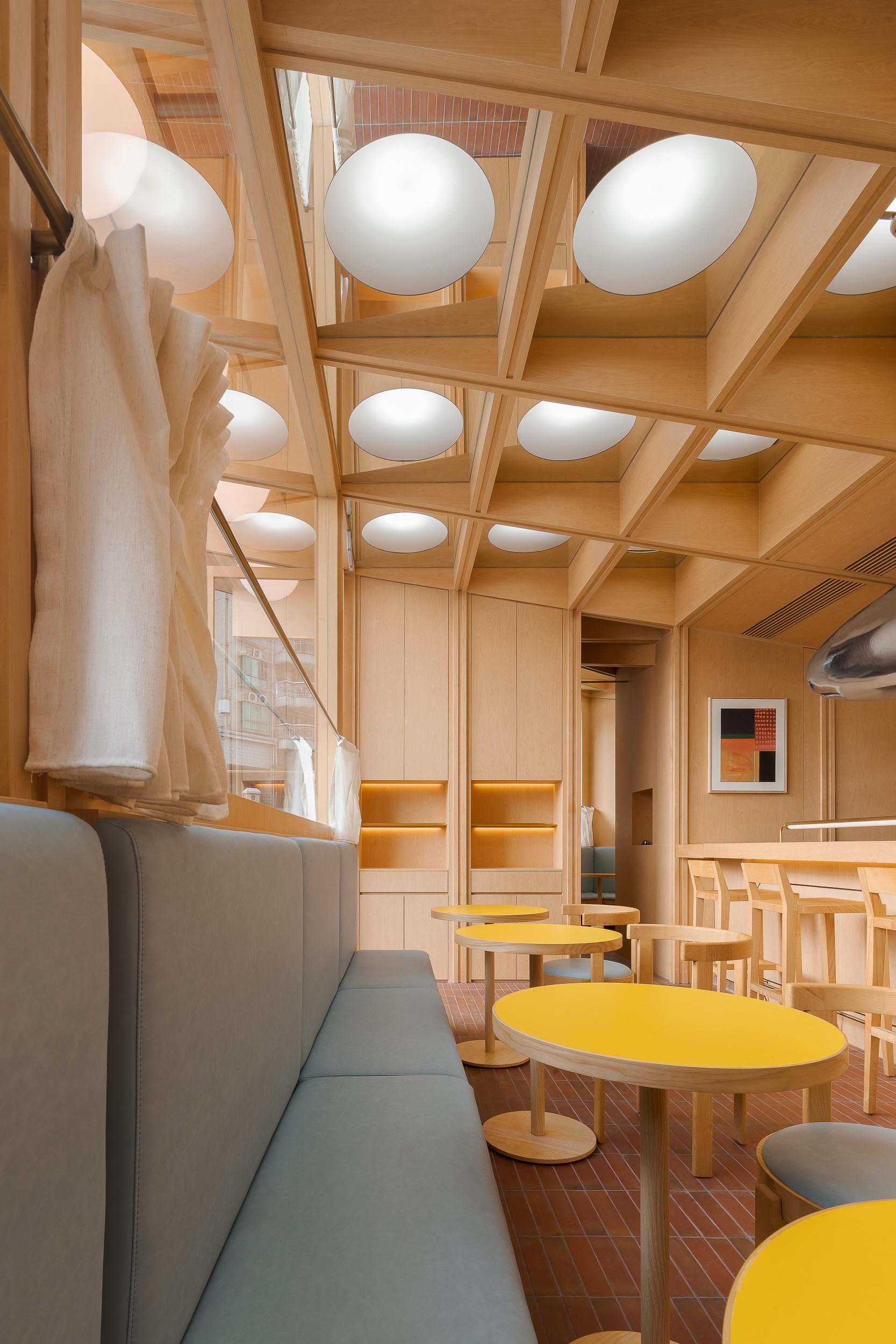 A modern cafe and bar with a wood interior, banquette seating, and bright yellow tables.