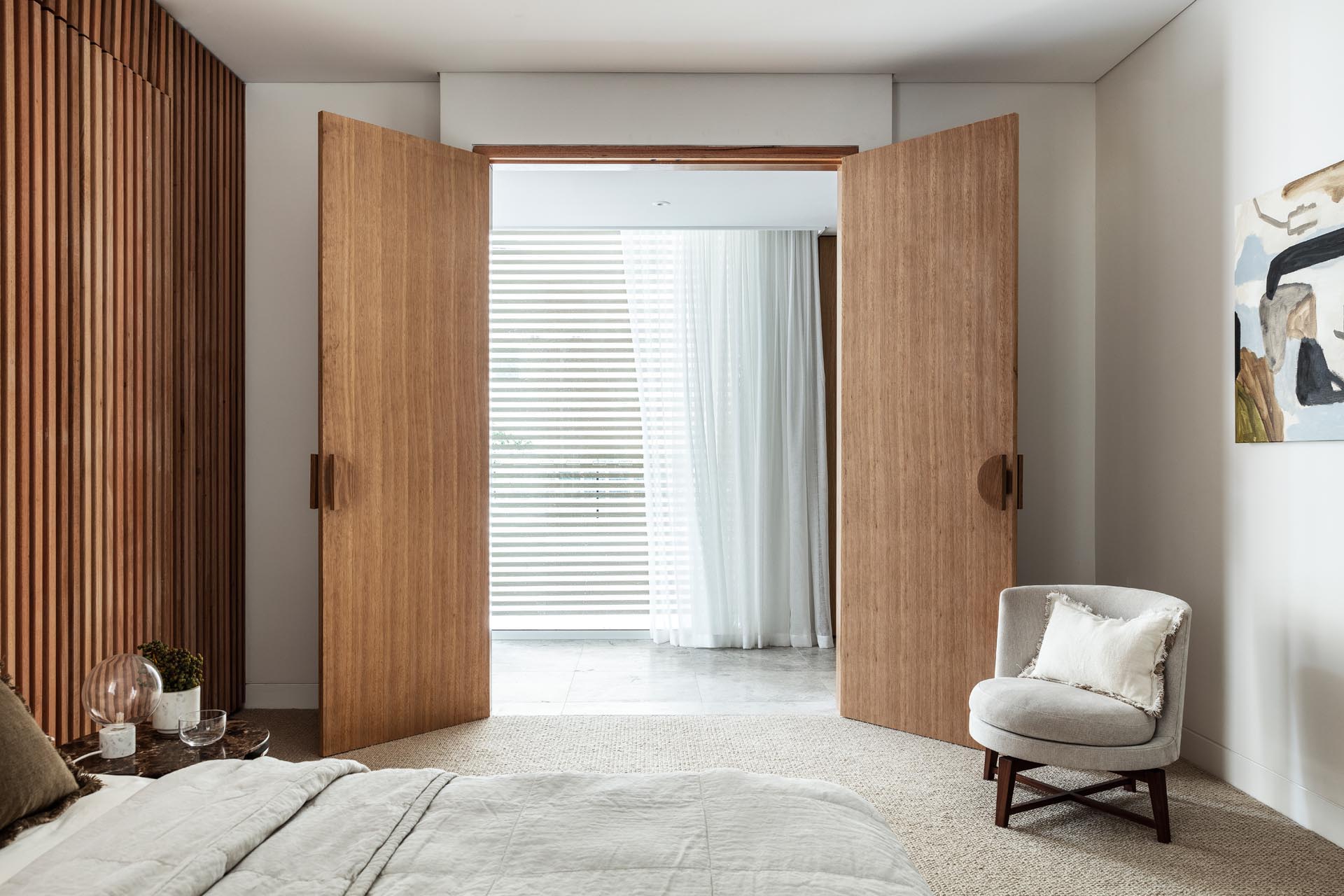 Two wood doors open to this modern bedroom, where a wood slat wall has been used to create an accent wall behind the bed.