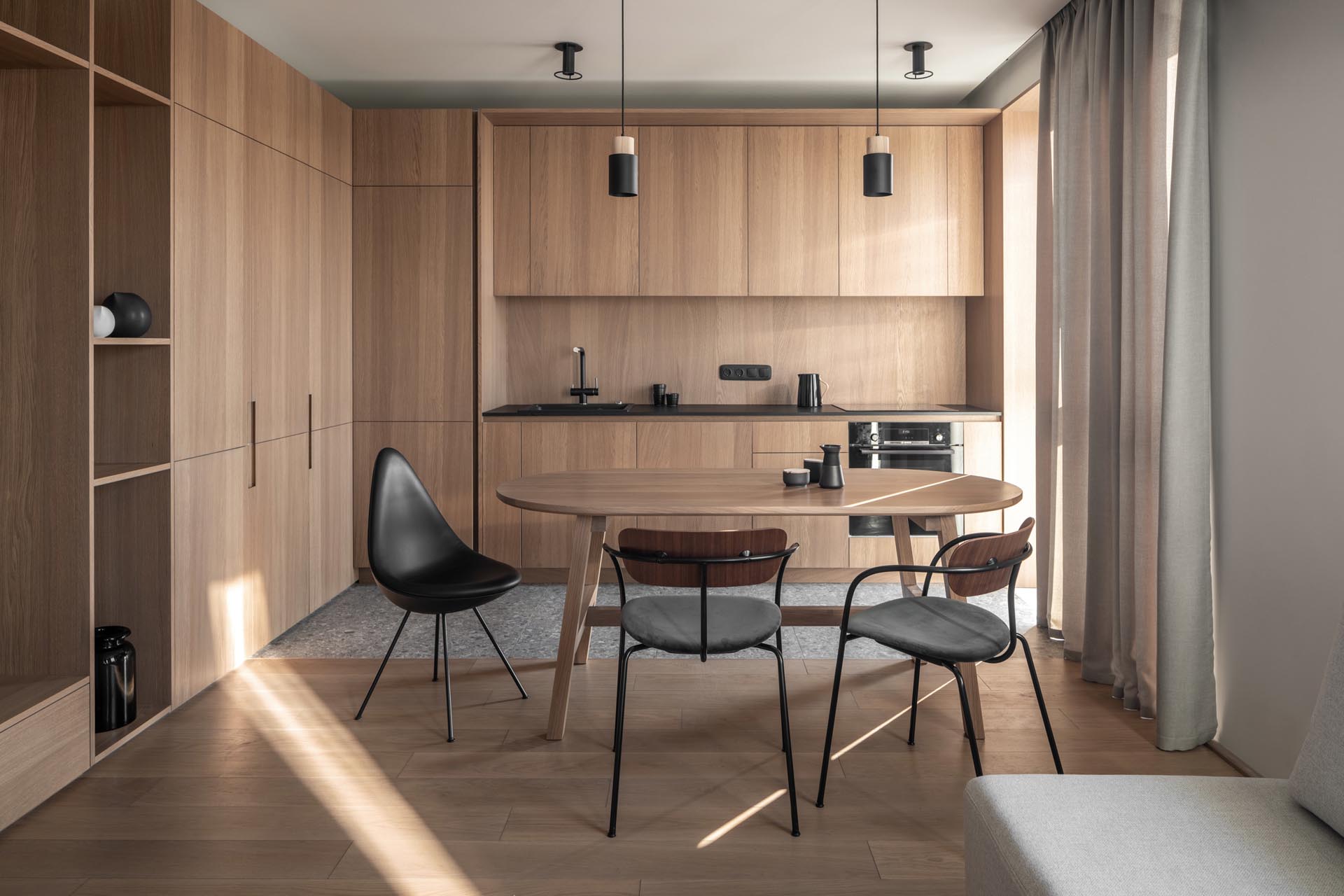 A modern wood kitchen with minimalist cabinets, black hardware, and an eat-in dining table.