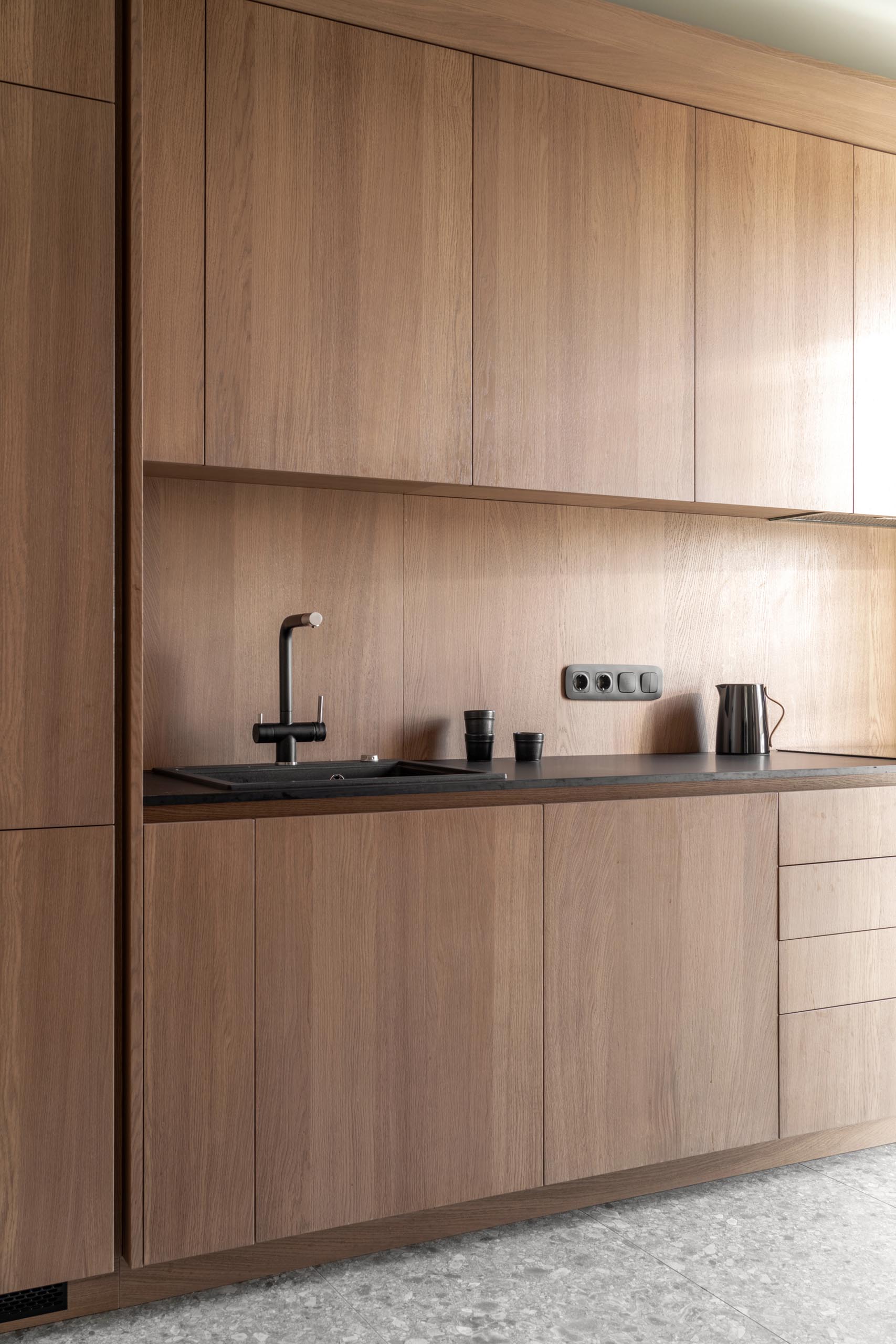 A modern wood kitchen with hardware-free cabinets, a dark countertop, and an integrated fridge and dishwasher.