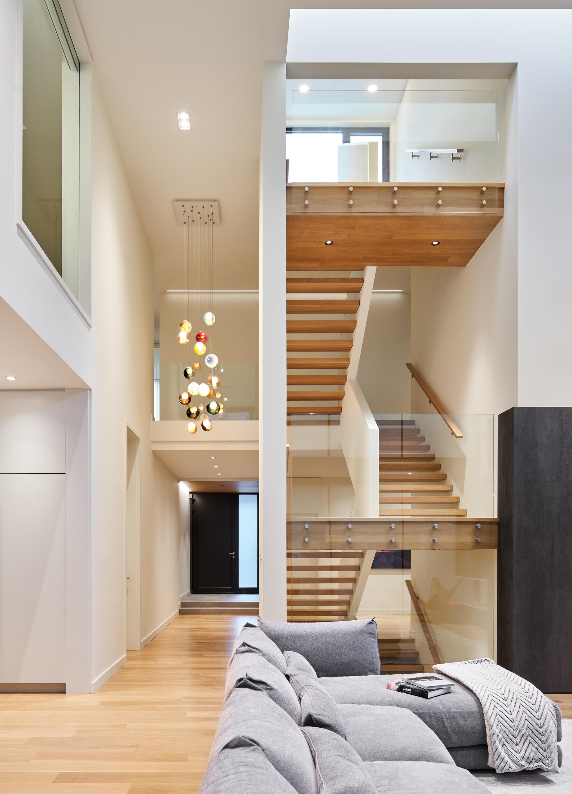 An open wood staircase with glass railings that connects the multiple levels of the home. A colorful accent has been added with the inclusion of suspended Bocci lights.