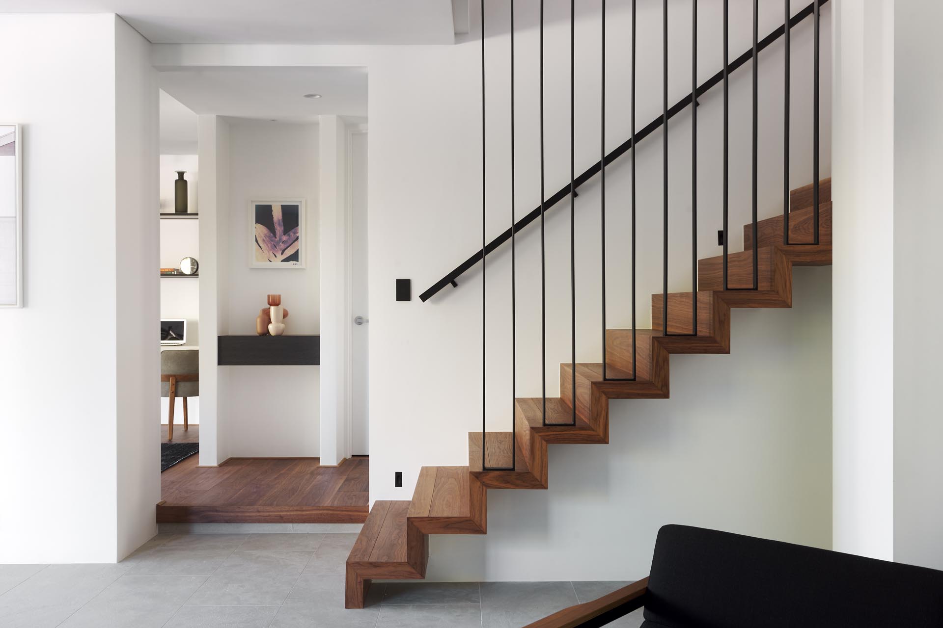 A modern house interior that includes wood stairs with a black metal railing that lead to the upper floor of the home.