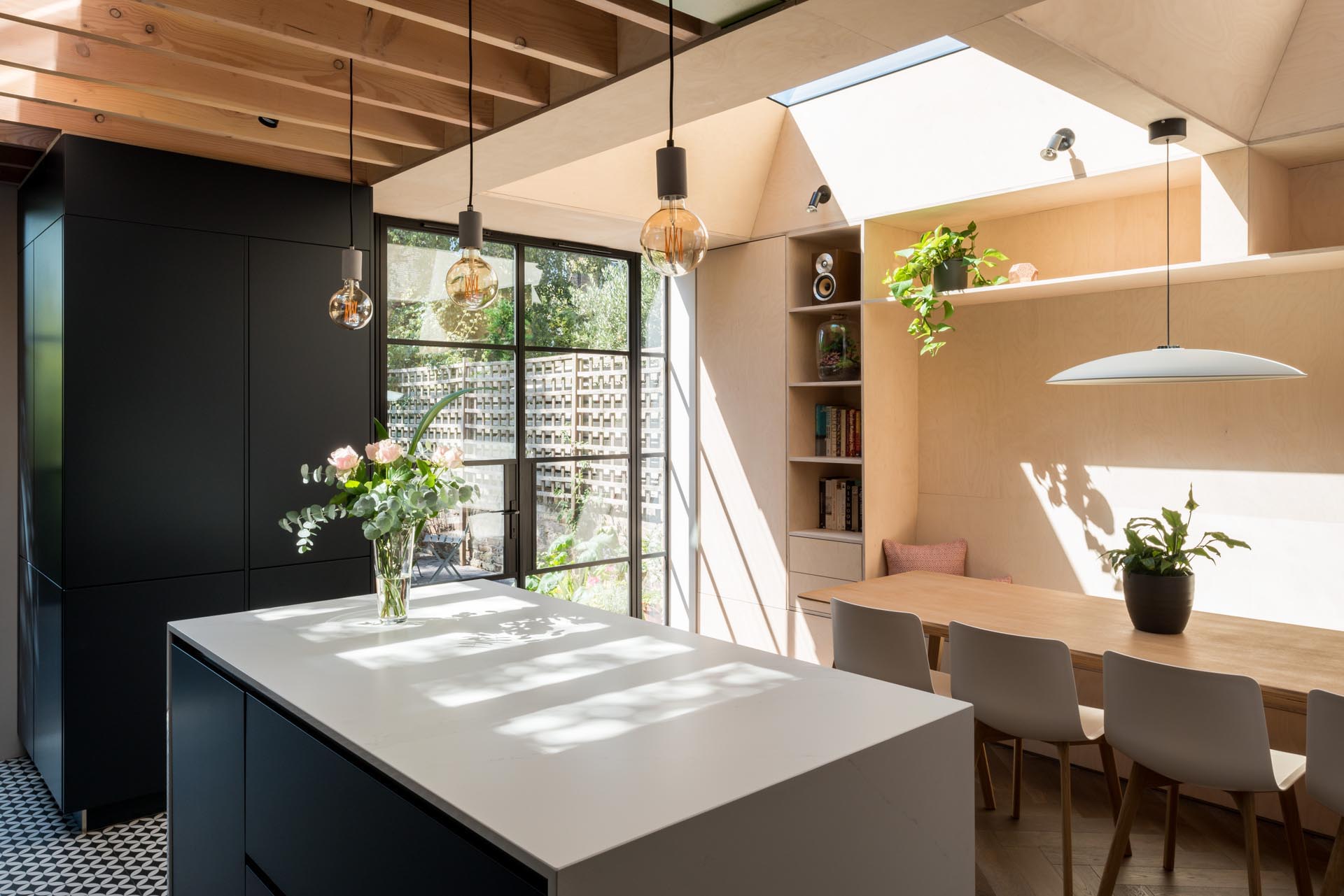 A new dining room has been designed with fitted storage, a long bespoke dining bench, plywood walls, Crittall doors, and two skylights.