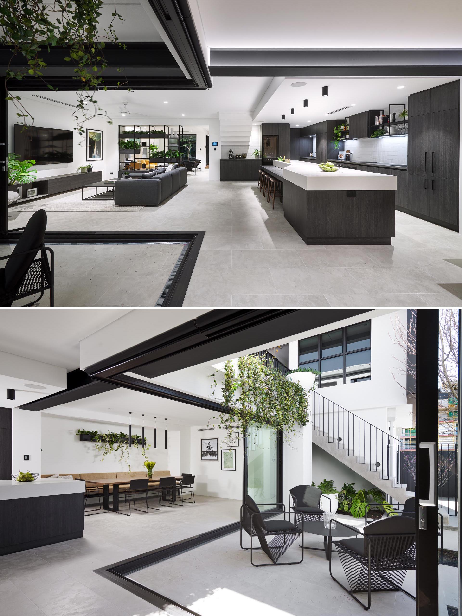 This modern house has retractable glass walls that open the interior spaces to a small outdoor courtyard. The dining room is adjacent to the kitchen and includes a long built-in banquette bench, a wall-mounted planter, and black dining chairs.