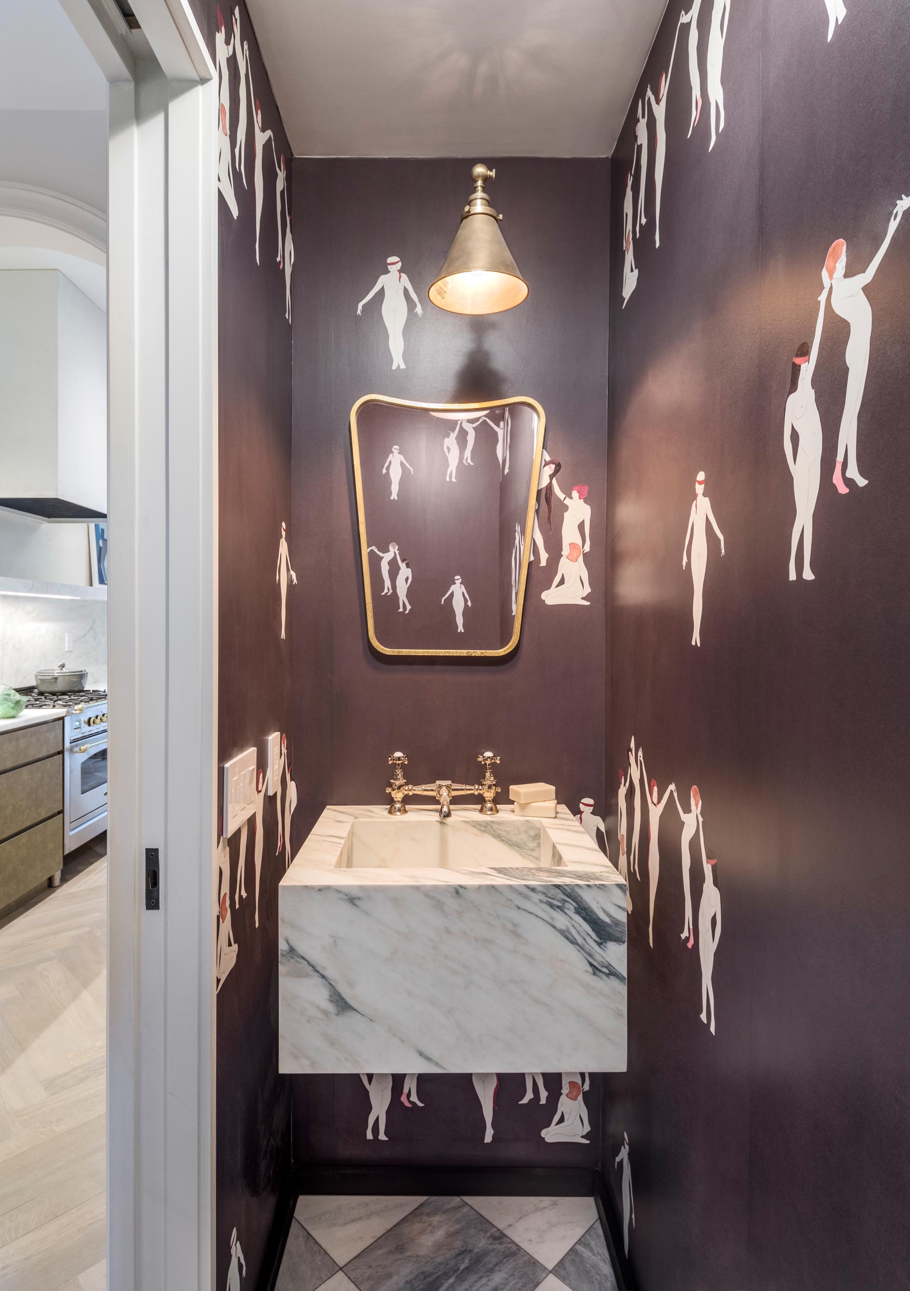 A powder room with gold accents, and black wallpaper that has pictures of women.