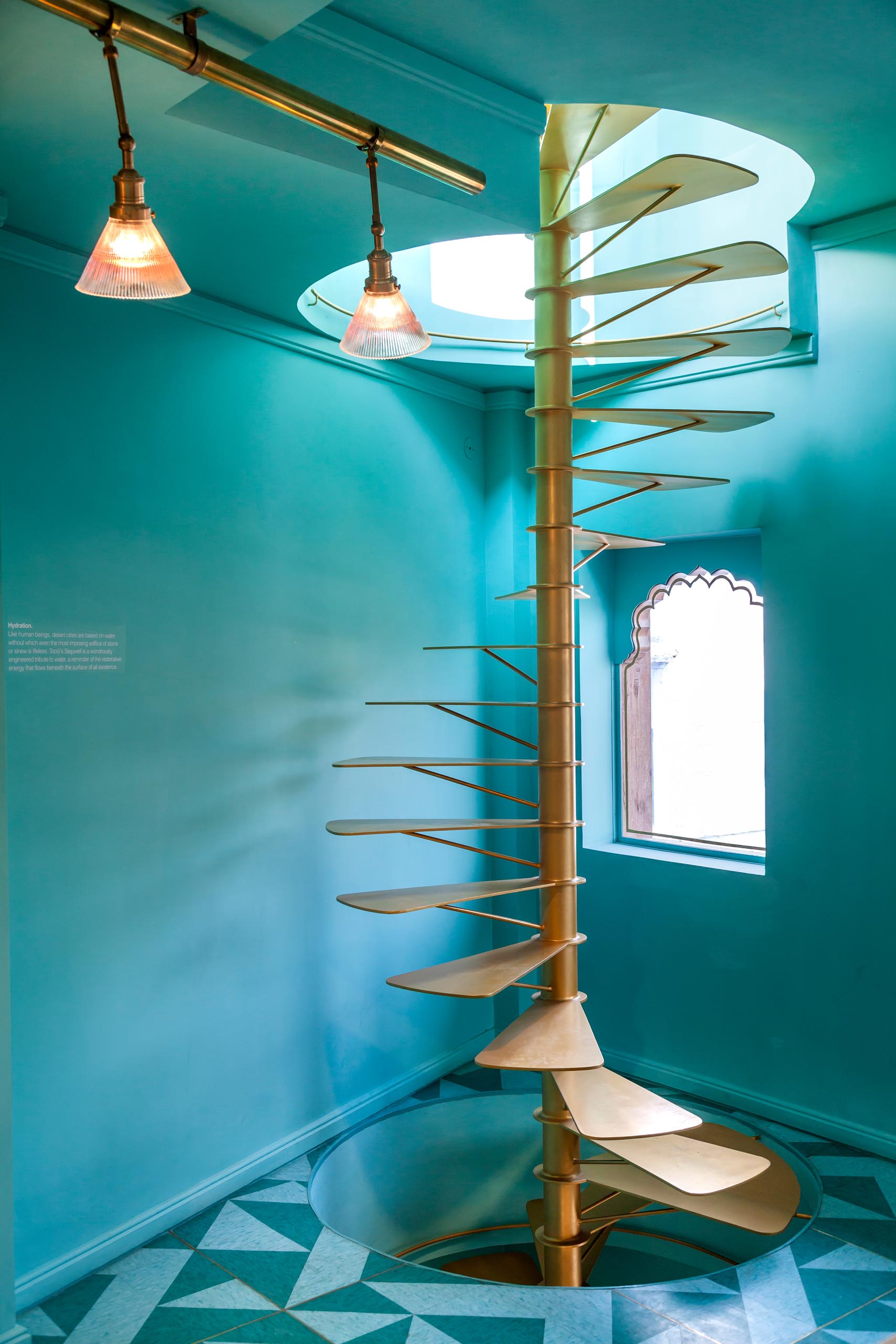 Teal blue/green walls surround a gold colored spiral staircase.