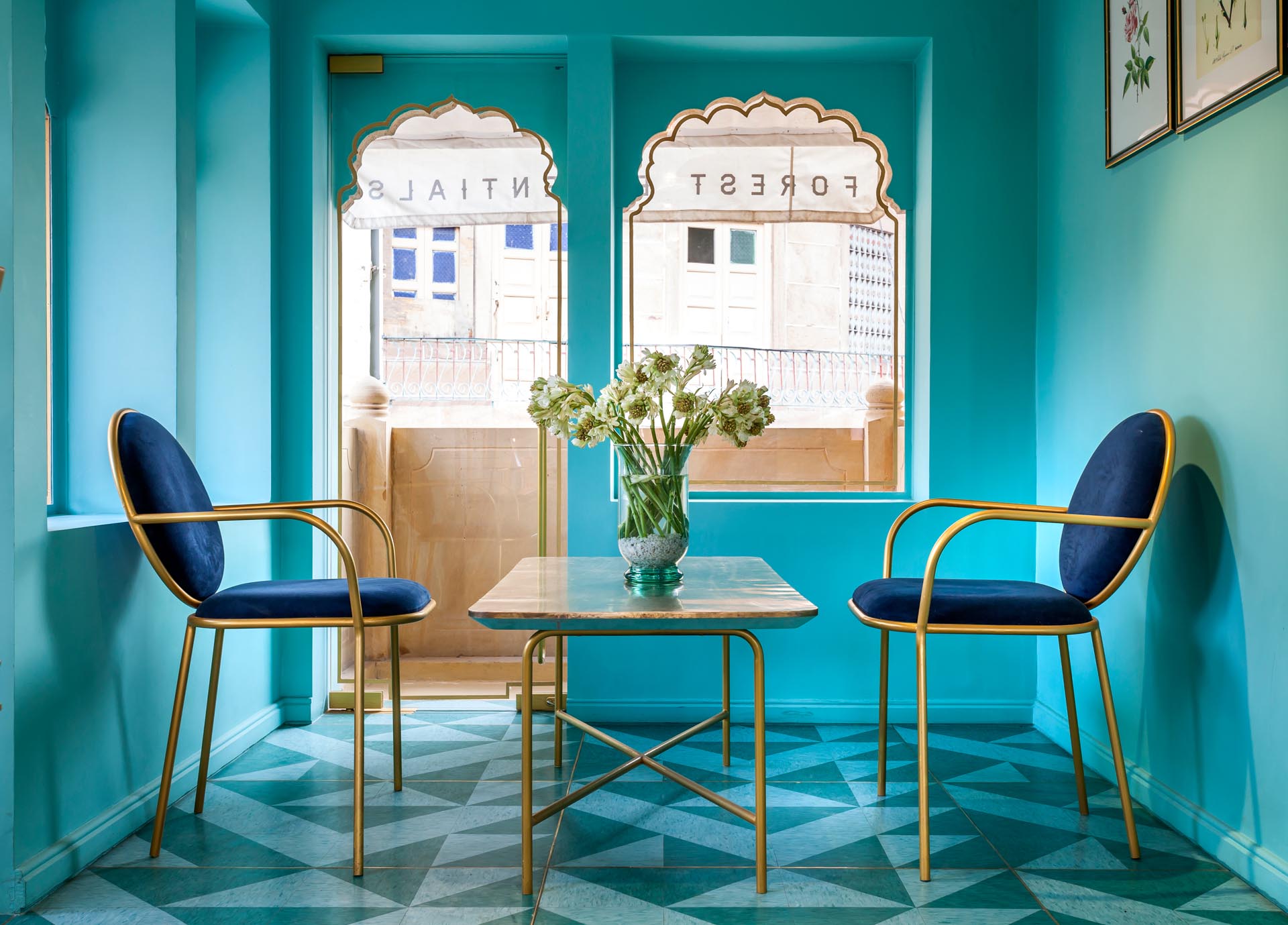 A modern retail store with teal walls, velvet chairs, and gold accents.