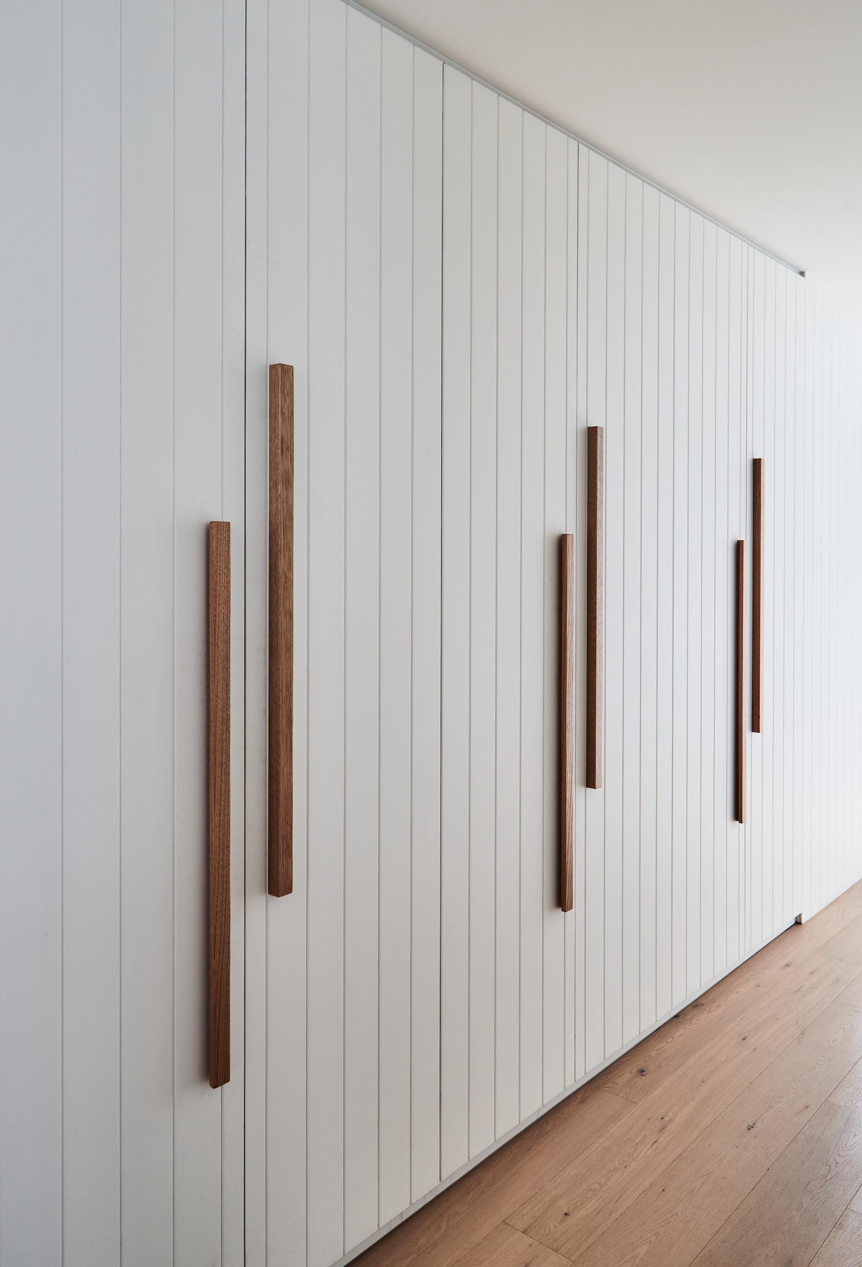 This hallway has plenty of storage space in the form of floor-to-ceiling white cabinets with contrasting natural wood hardware.