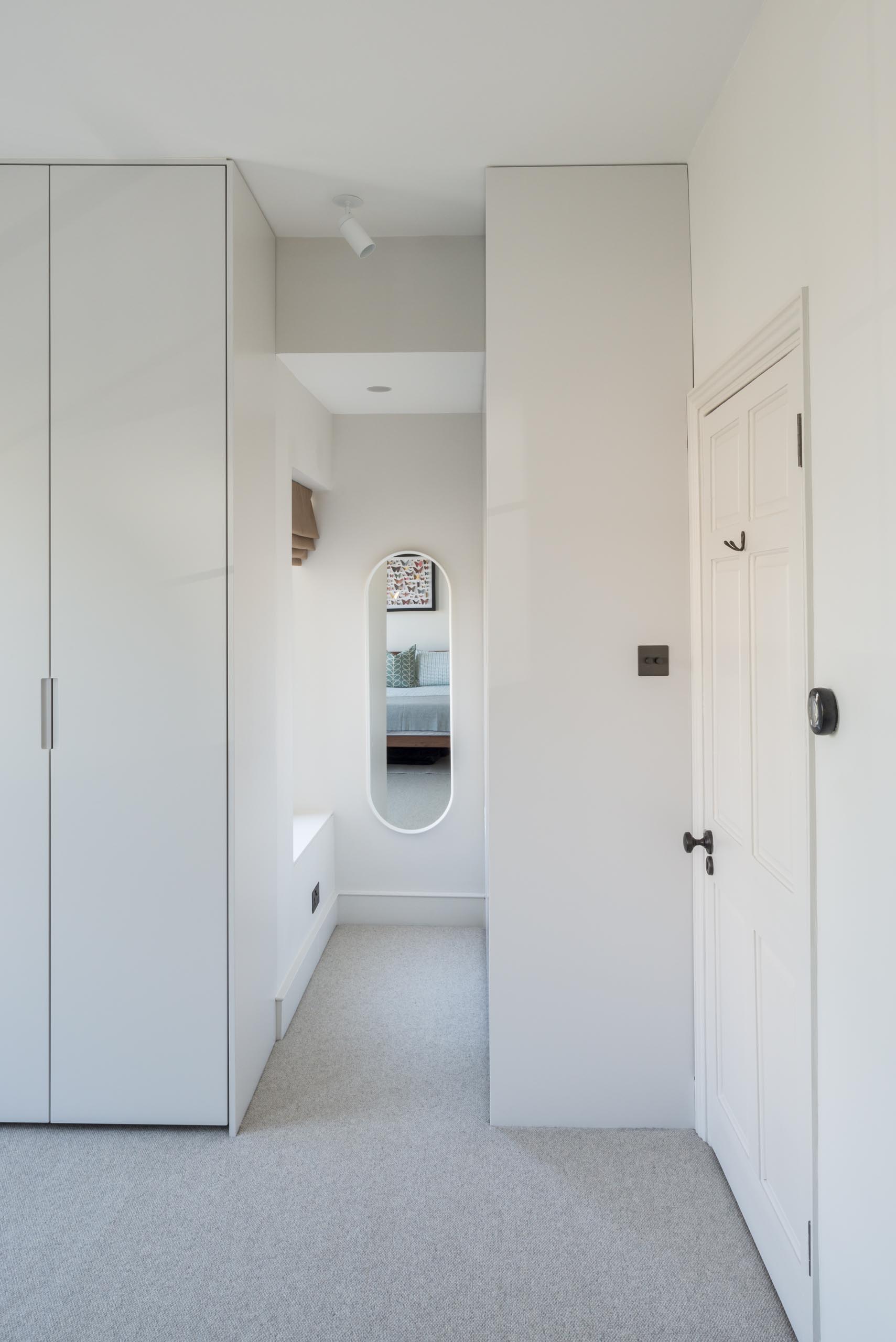 A modern walk-in closet with wood cabinets and a pill-shaped mirror.