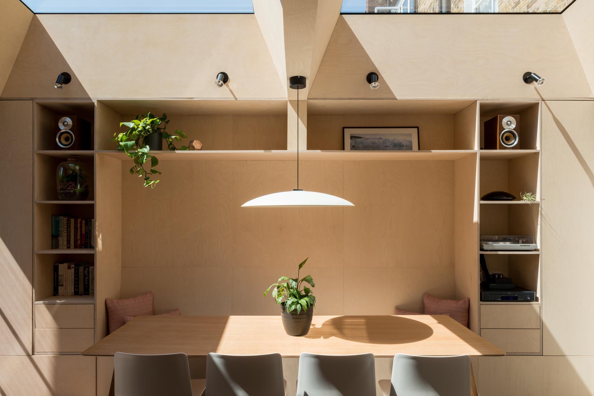 A new dining room has been designed with fitted storage, a long bespoke dining bench, plywood walls, and two skylights.