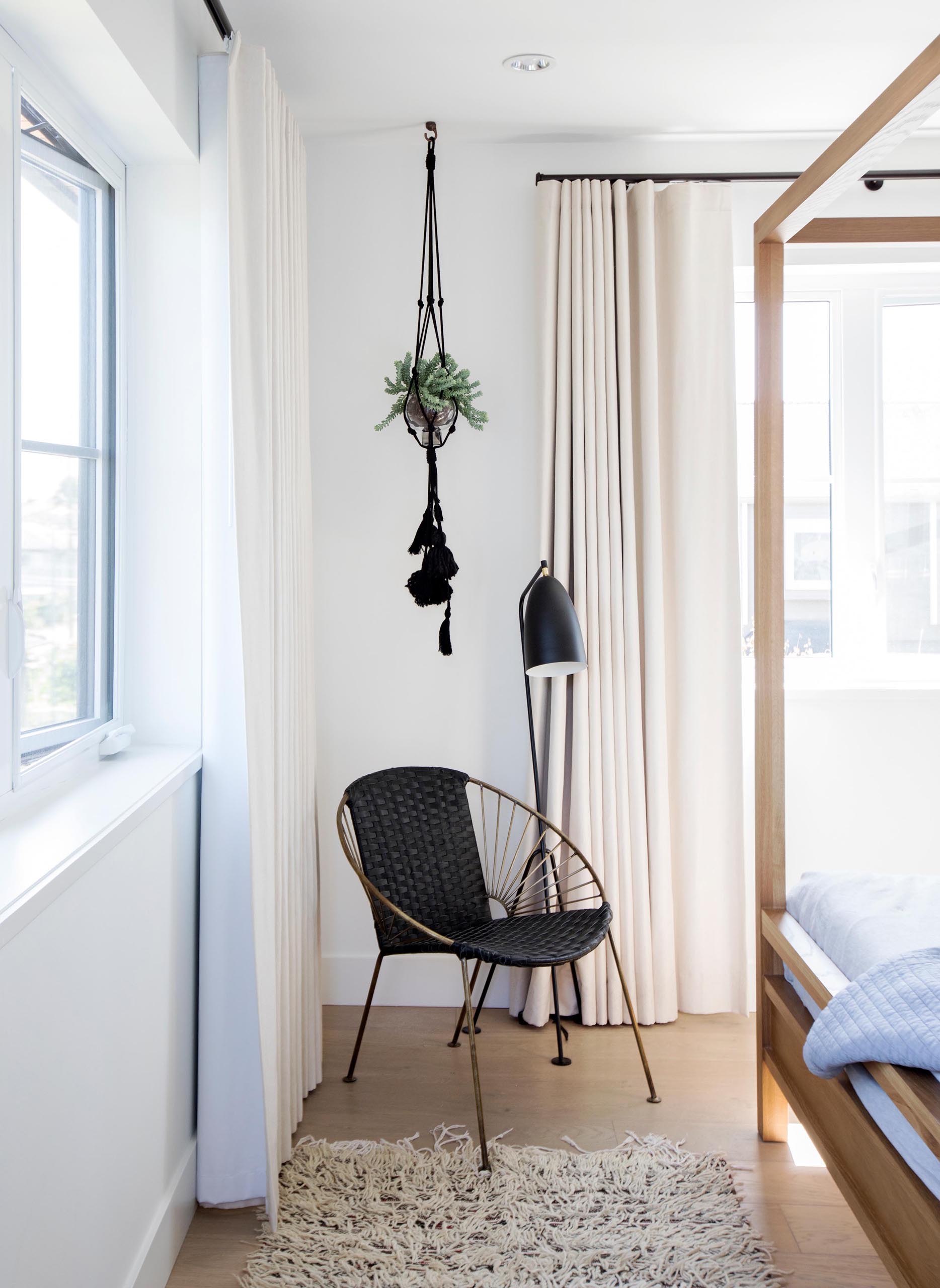 A modern bedroom with a black accent corner furnished with a hanging plant, black floor lamp, and black chair.