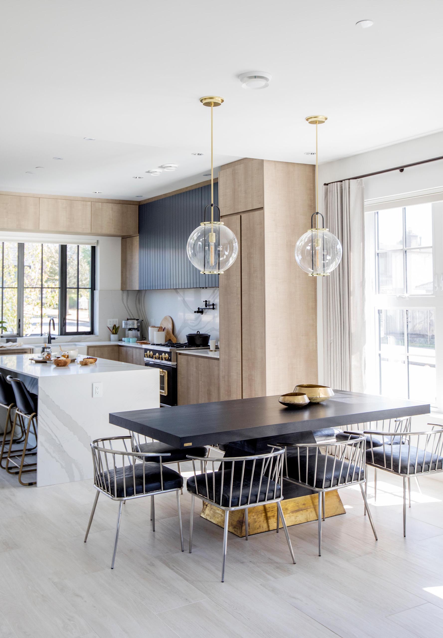 A black dining table with gold accents, is anchored in the open floor plan by two glass pendant lights.