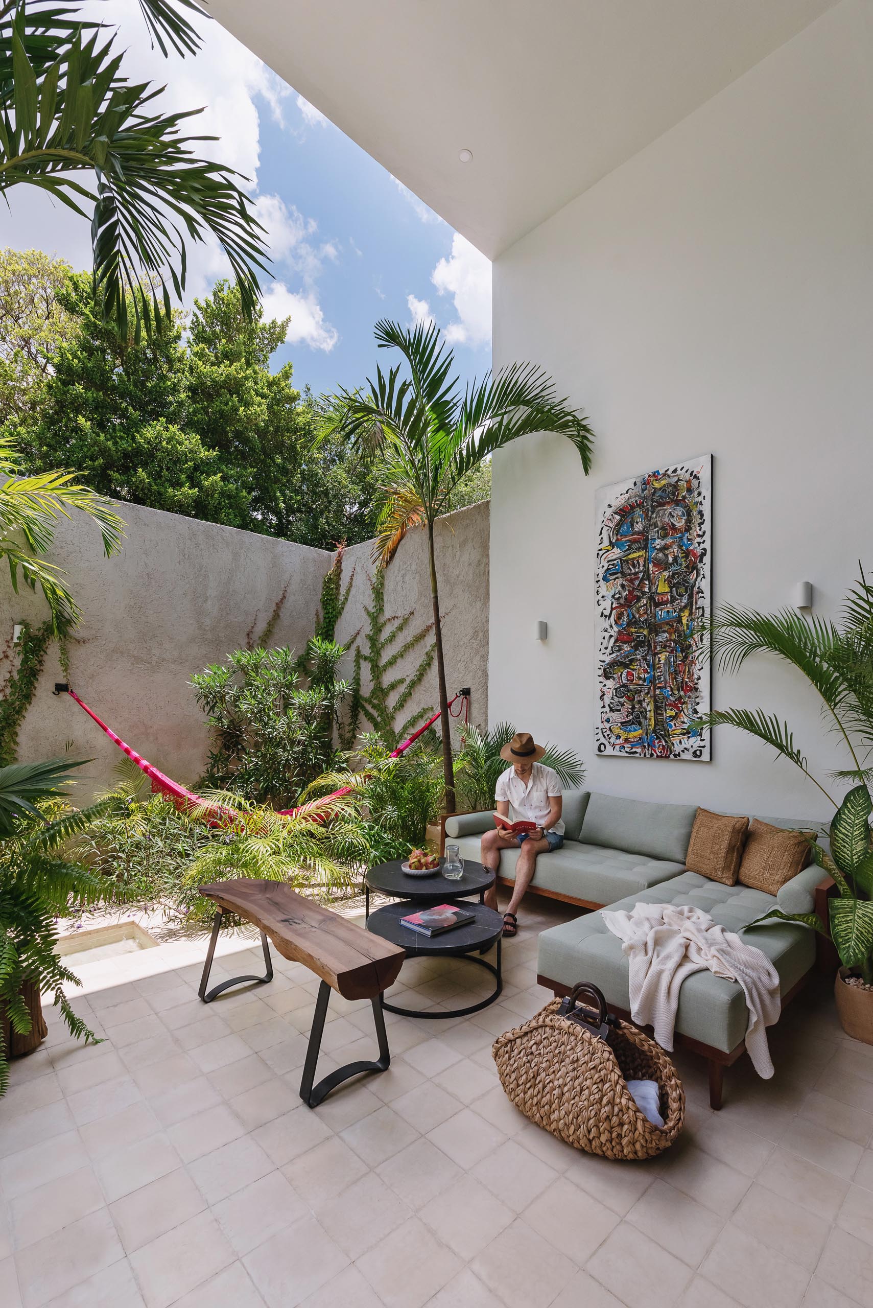 An outdoor living room with a comfortable sofa and a hammock surrounded by tropical plants.