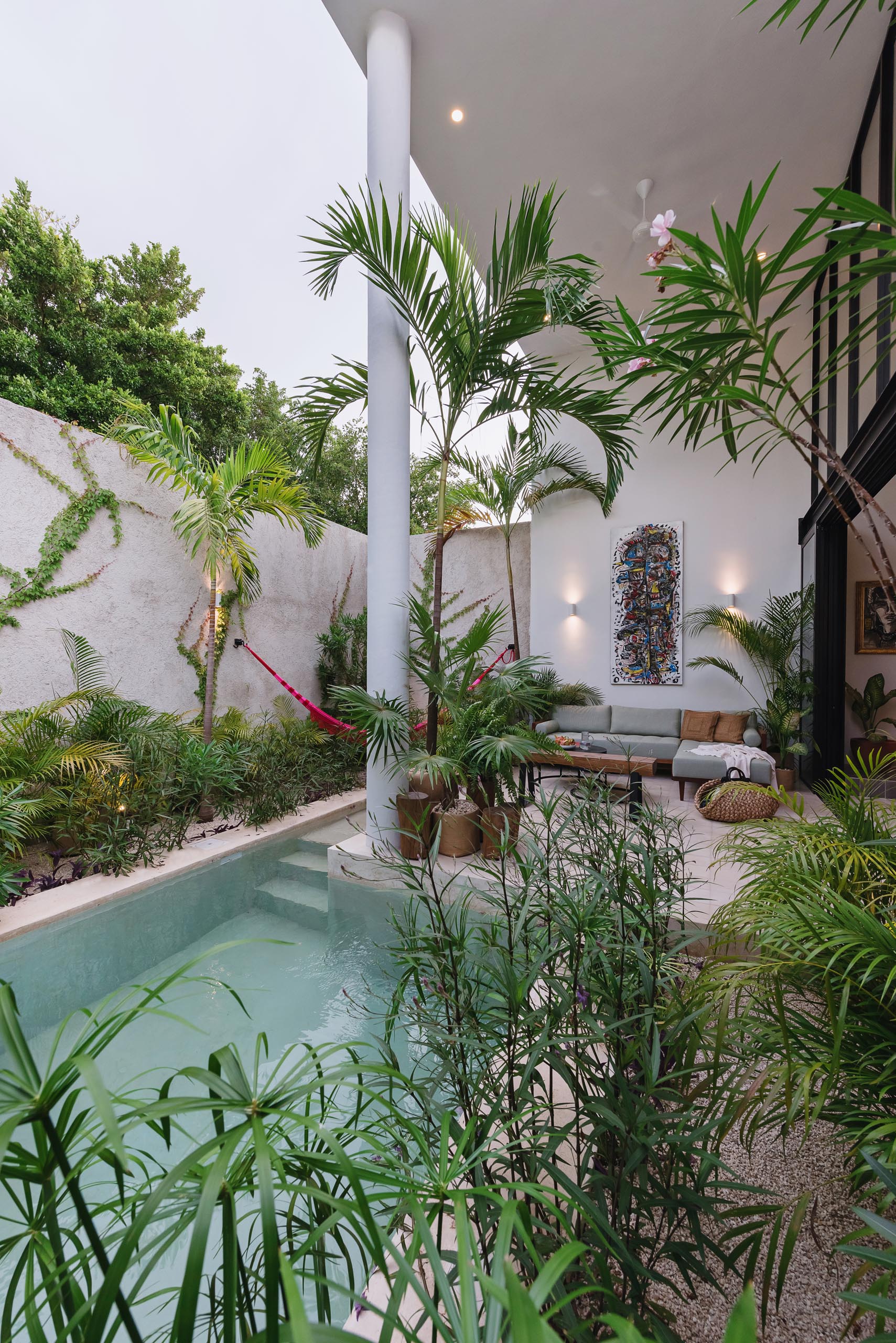 A small house with an outdoor living room, tropical plants, and small pool.