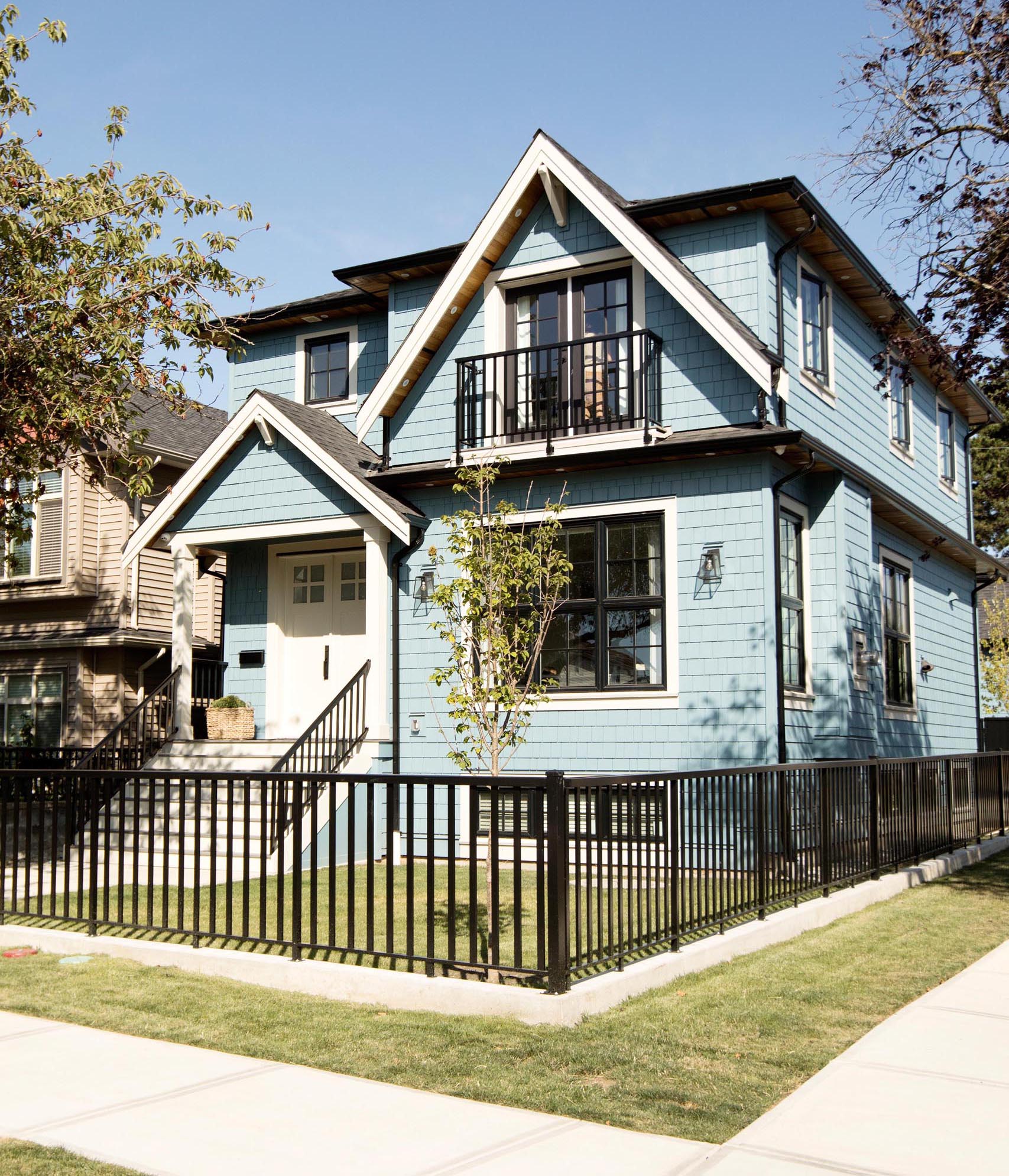 A contemporary light blue house with white trim and contrasting black fence, railings, and window frames.