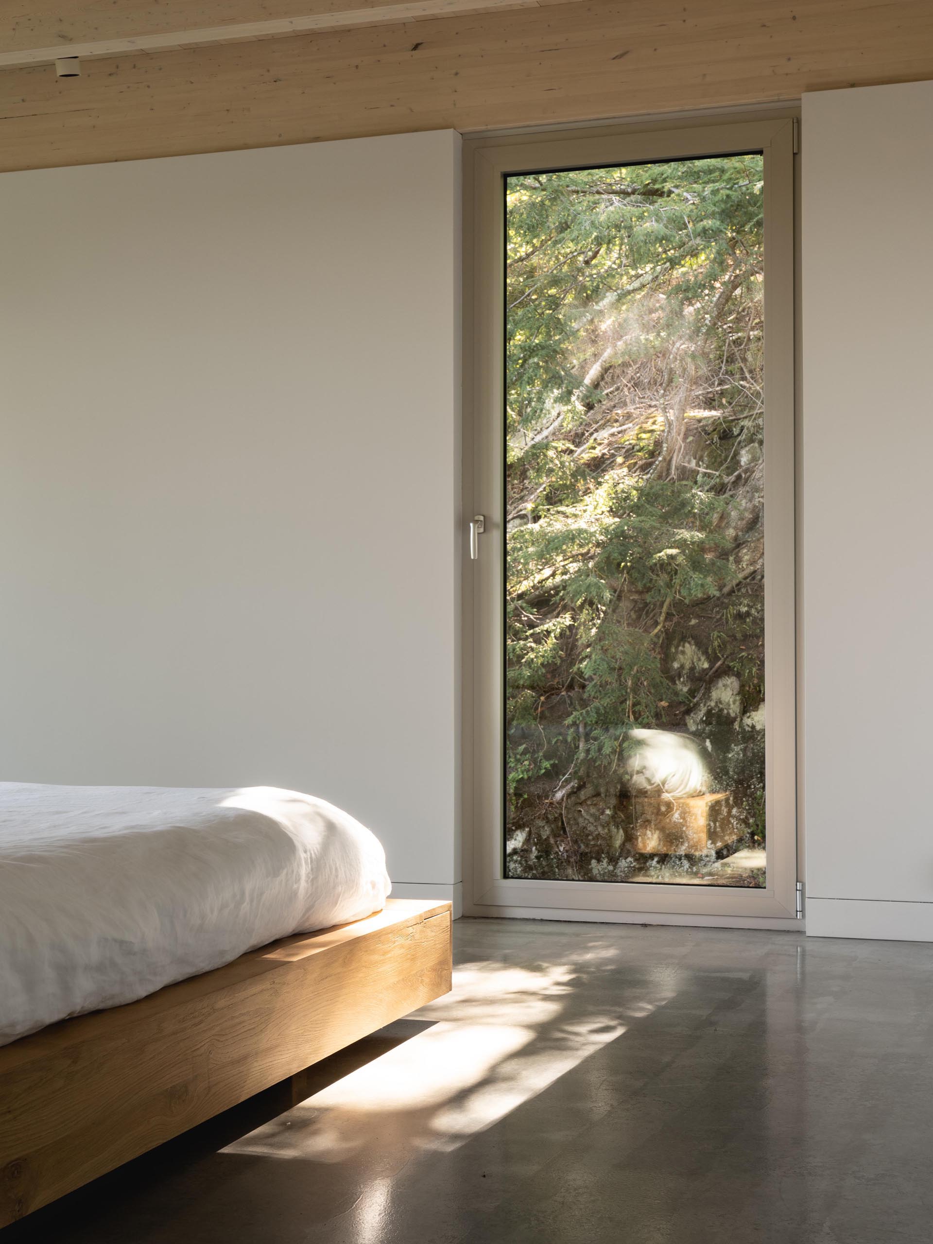 A tall window provides this modern bedroom with views of the forest.