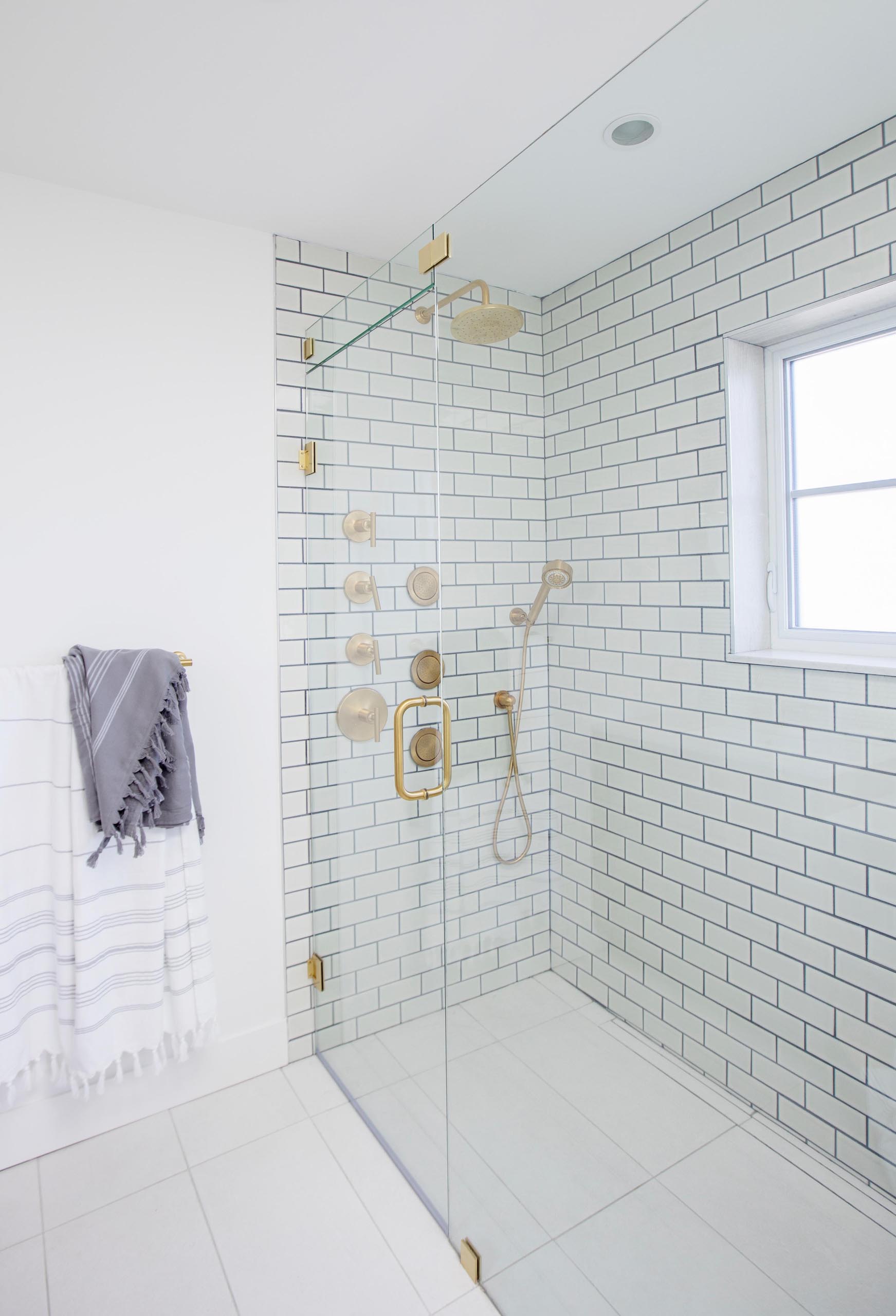 A modern shower with gold hardware, white subway tiles, and contrasting dark grout.