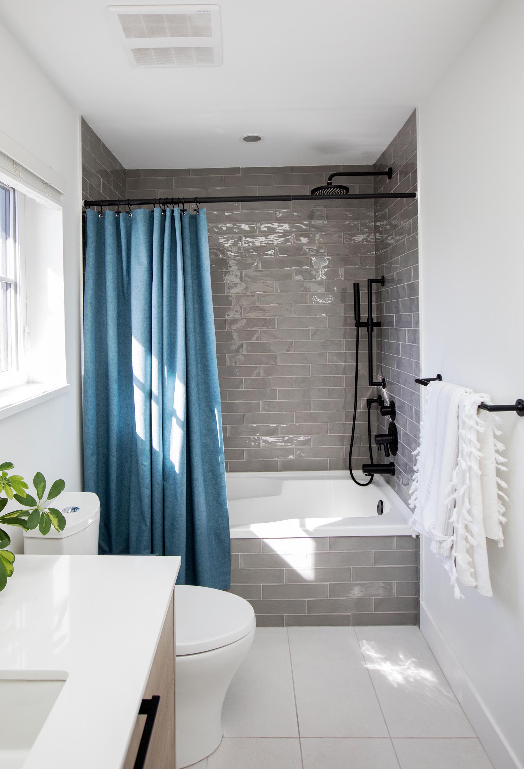 A modern bathroom with a gray-tiled shower, black hardware, and blue shower curtain.