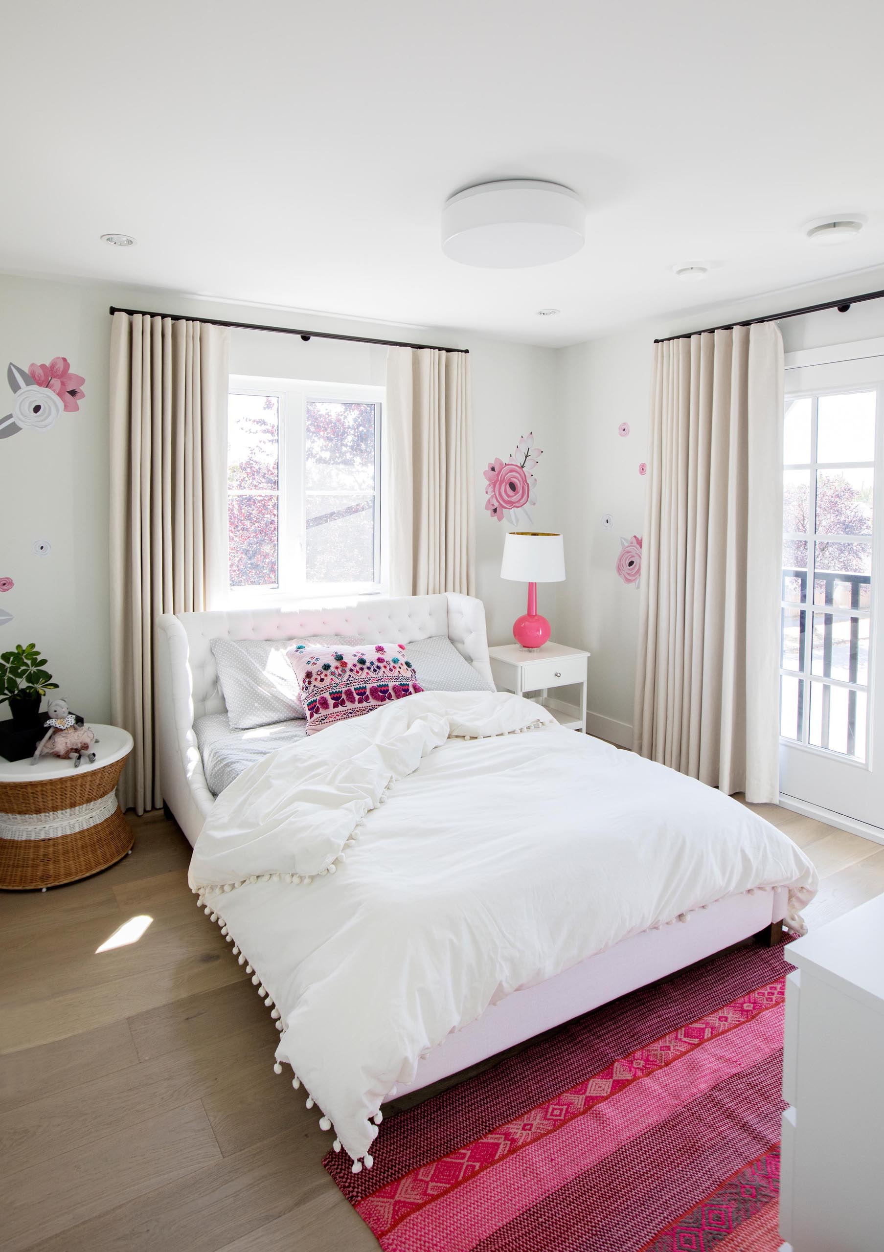 In this bedroom, a pink and white color palette has been chosen. Floral accents adorn the walls, and a striped pink rug is located at the end of the bed, 