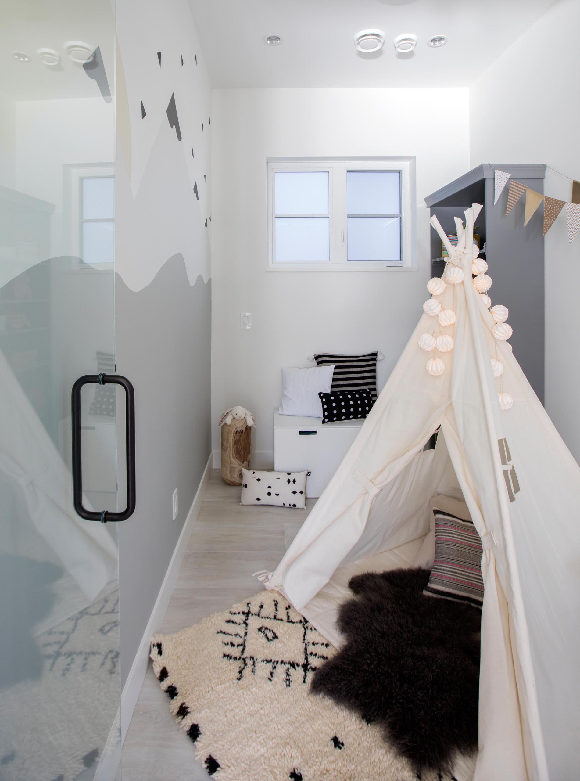 A modern play room with a mountain wall mural, tent, and shelving has been created in a small room.