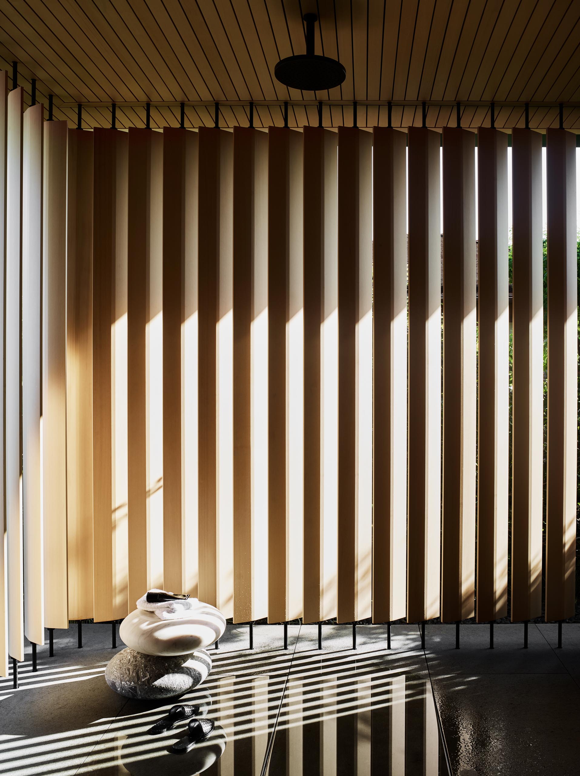 In this master bathroom, large format gray tiles cover the floor, vertical wood screens create privacy, and a white double-sink vanity floats above the ground and is adjacent to the glass-enclosed shower.