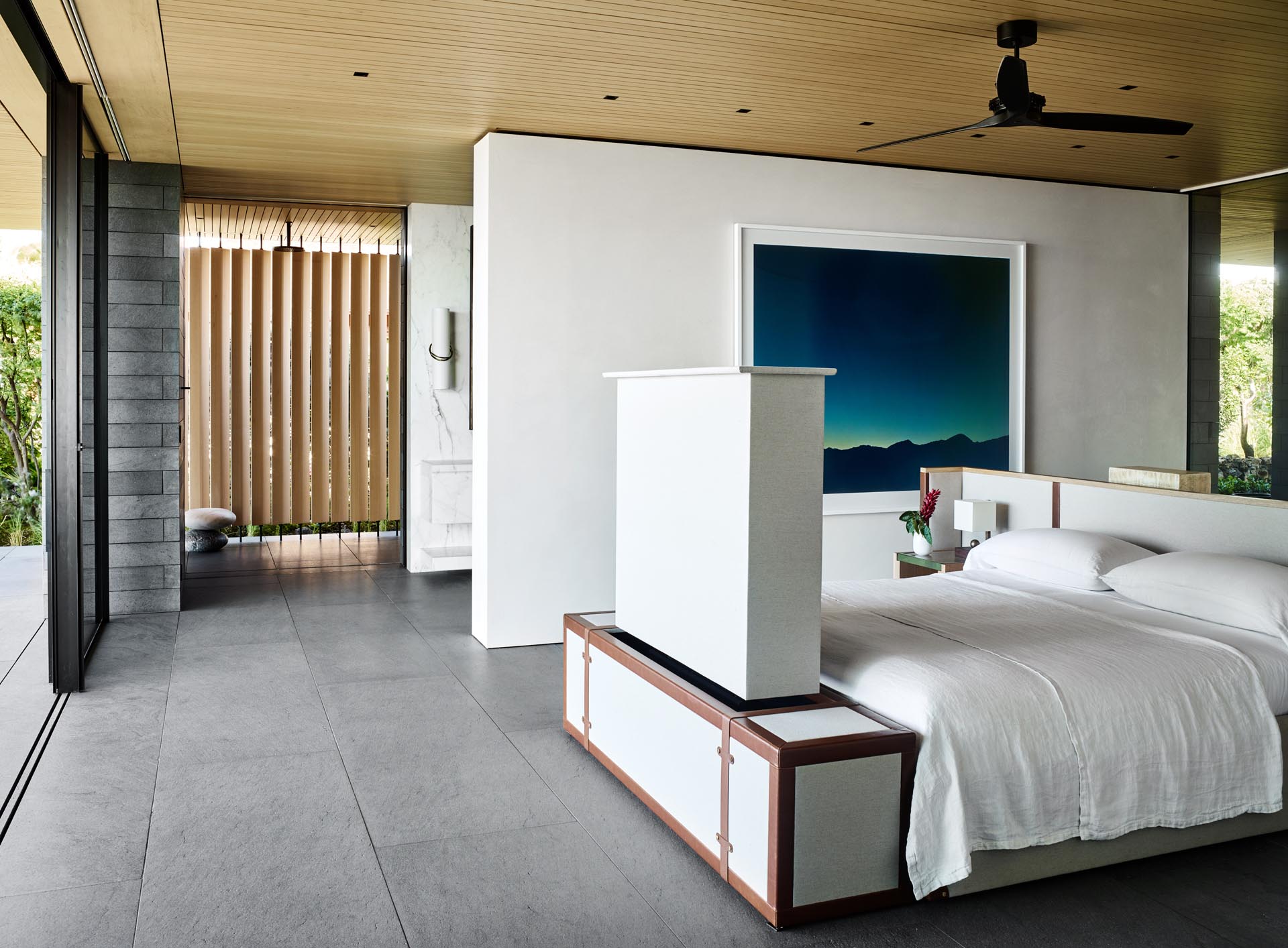 In the master bedroom, the bed frame has been centrally positioned in the room to take advantage of the views. There's also a hidden television at the end of the bed, and behind the headboard, there's a desk.