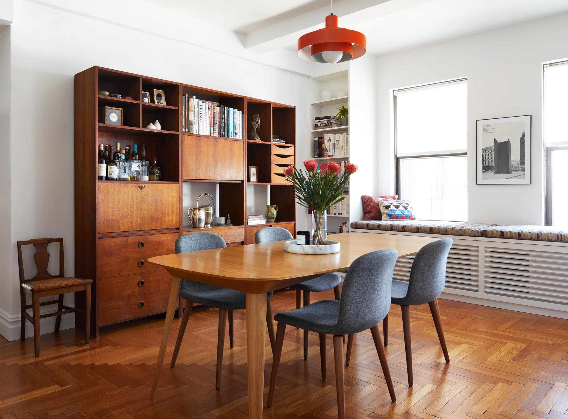 A remodeled dining room includes a deep orange pendant light from the the 1960s, a custom reading bench by the windows, and a vintage Danish media cabinet