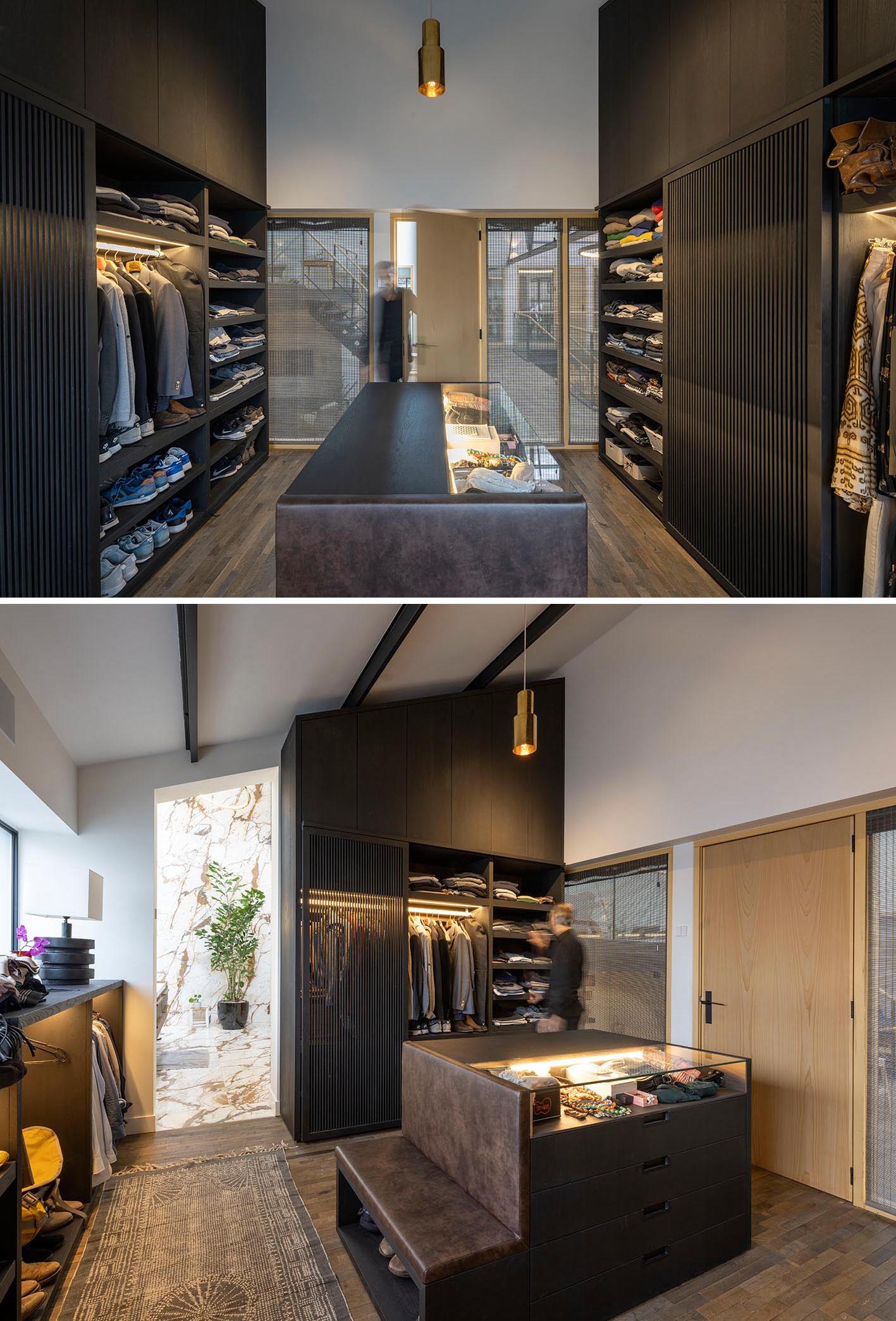 A modern walk-in closet with black cabinets, a central accessories island, and plenty of open shelving.