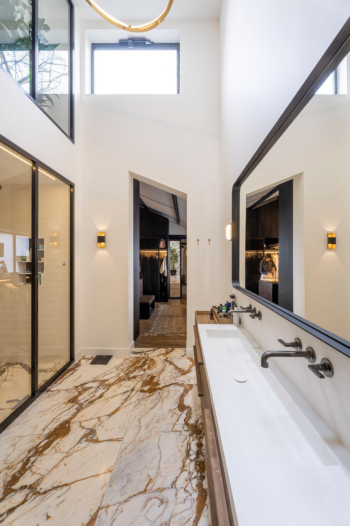 A modern bathroom with a glass-enclosed shower and a long thin vanity with a trough sink.