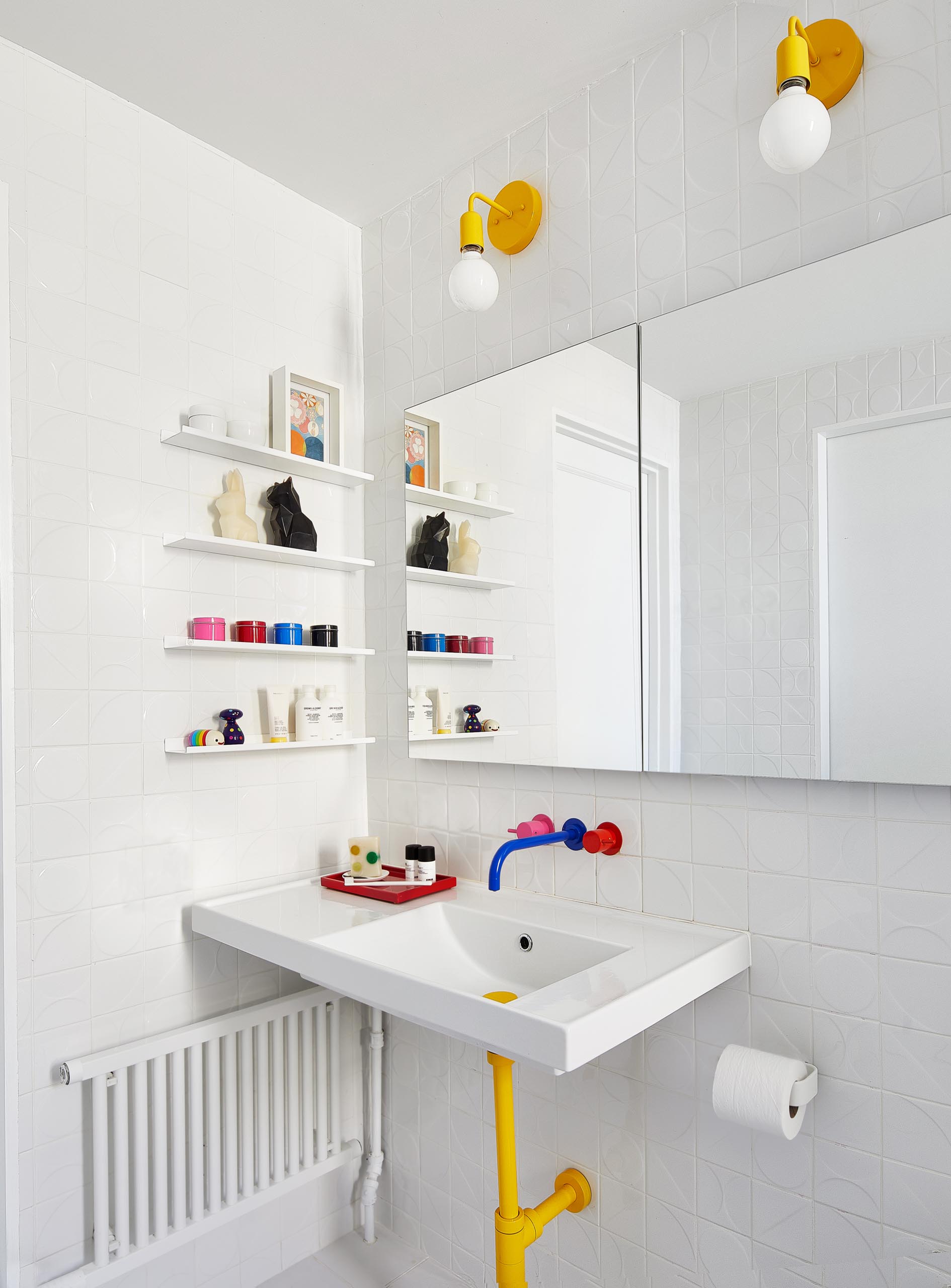 In this kids’ bathroom, mix-and-match hot pink, yellow, and blue plumbing fixtures by VOLA join dimensional wall tiles by Kho Liang and yellow lighting fixtures from Barn Lighting.